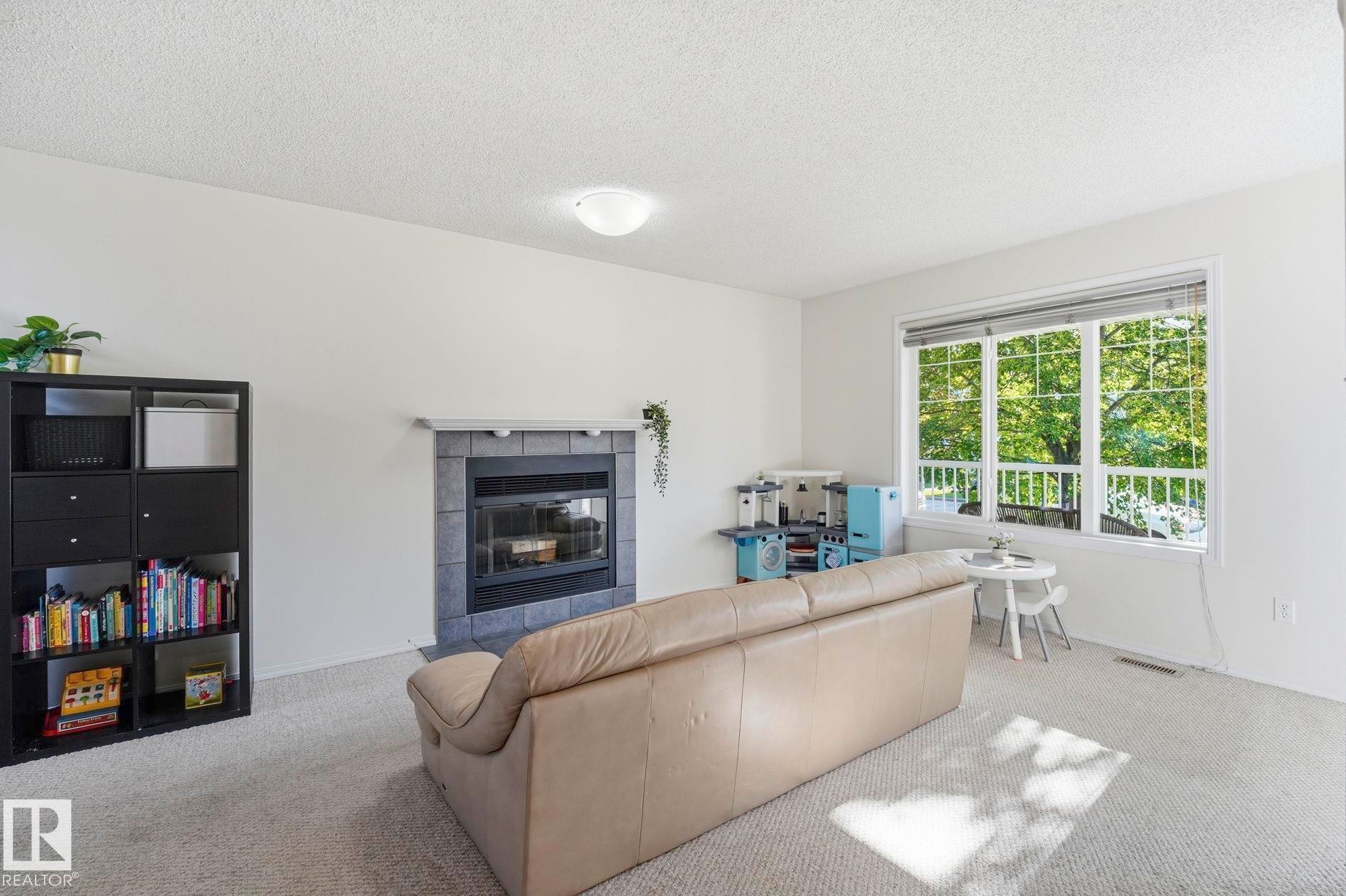 Carpeted living area featuring a central fireplace with a dark tile surround and a light-colored mantel - 215 85 Street Sw, Edmonton, AB - Indoor Photo Showing Other Room With Fireplace