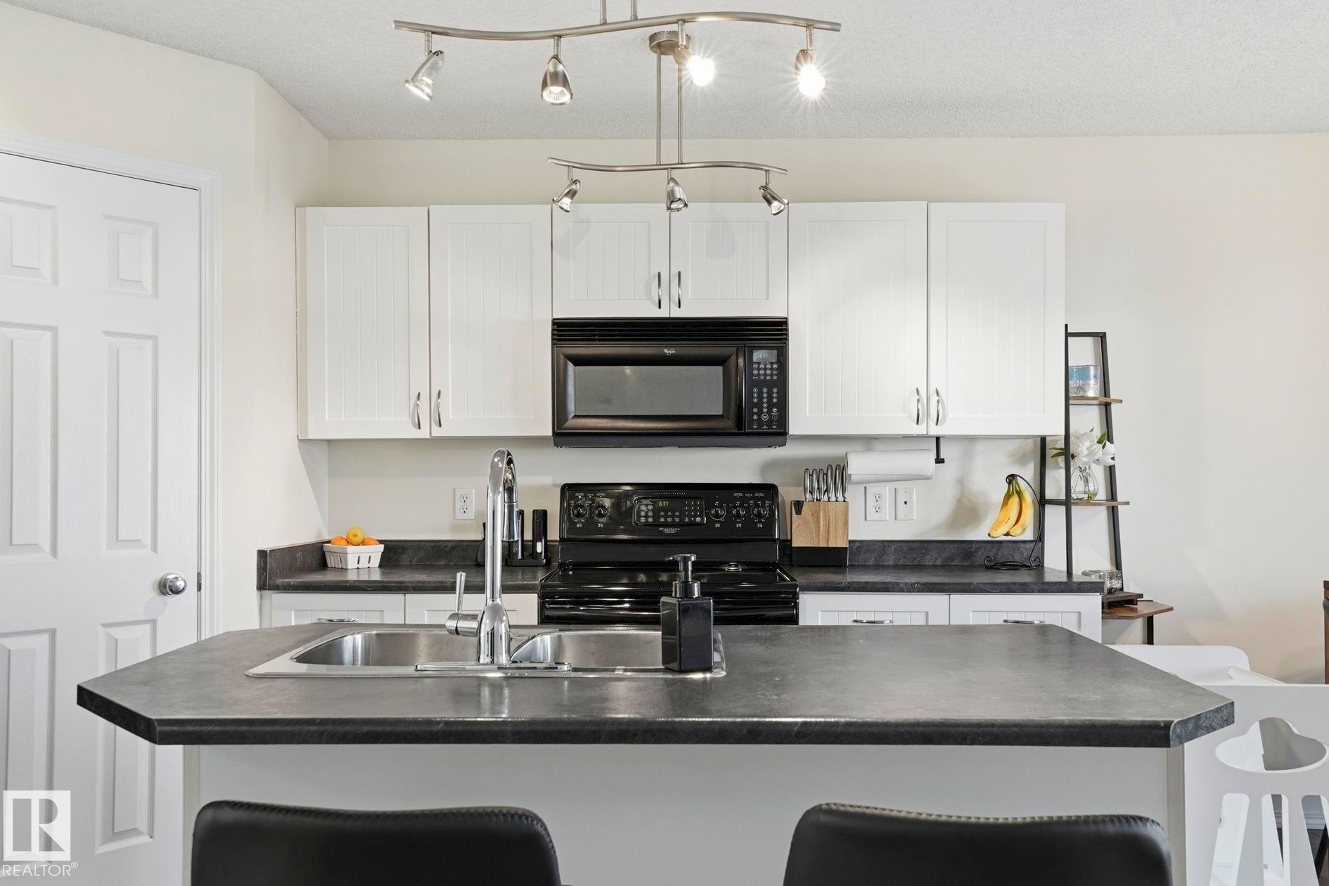 Kitchen featuring an island with a double basin sink, white cabinetry, and contrasting dark countertops - 215 85 Street Sw, Edmonton, AB - Indoor Photo Showing Kitchen With Double Sink