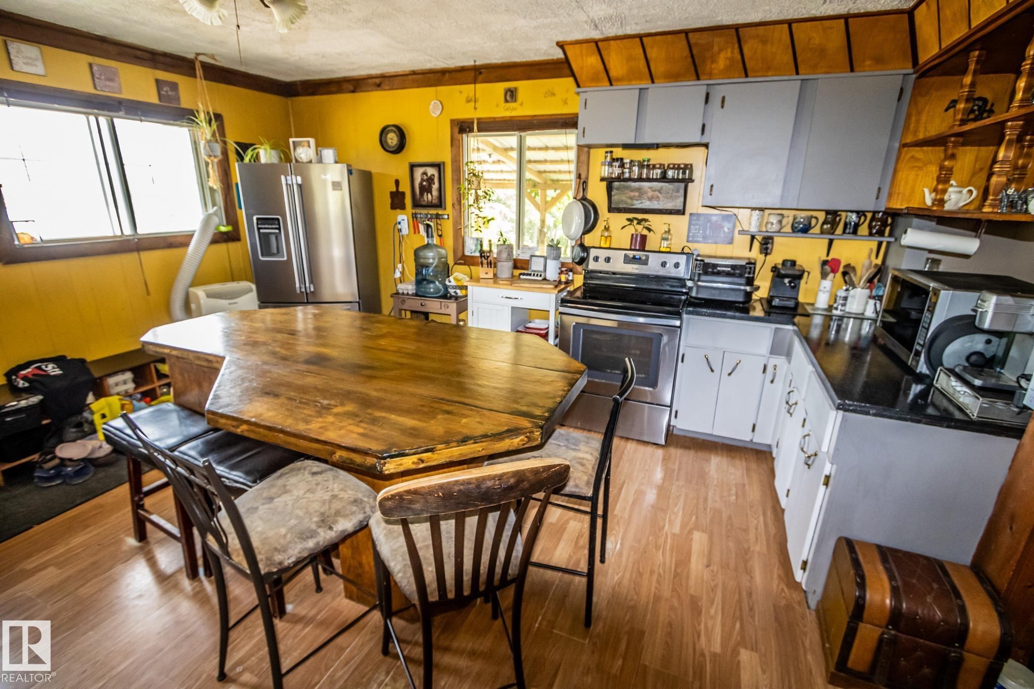 Bright, open-concept kitchen and dining area featuring warm yellow walls, wood-finish flooring throughout, and a large octagonal dining table - 11218 Twp Rd 590, Rural St. Paul County, AB - Indoor