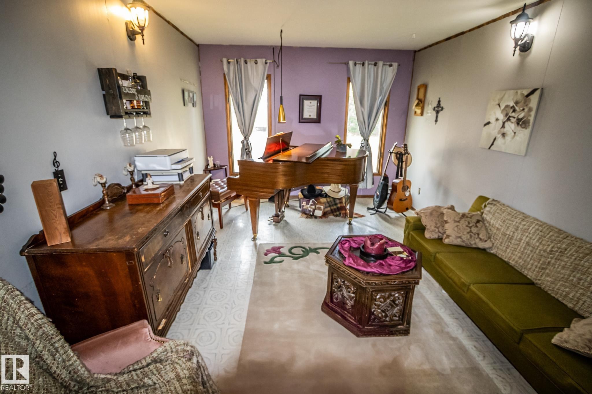 Spacious room featuring light-toned flooring, dual wall sconces, and a large window with drapes - 11218 Twp Rd 590, Rural St. Paul County, AB - Indoor Photo Showing Living Room