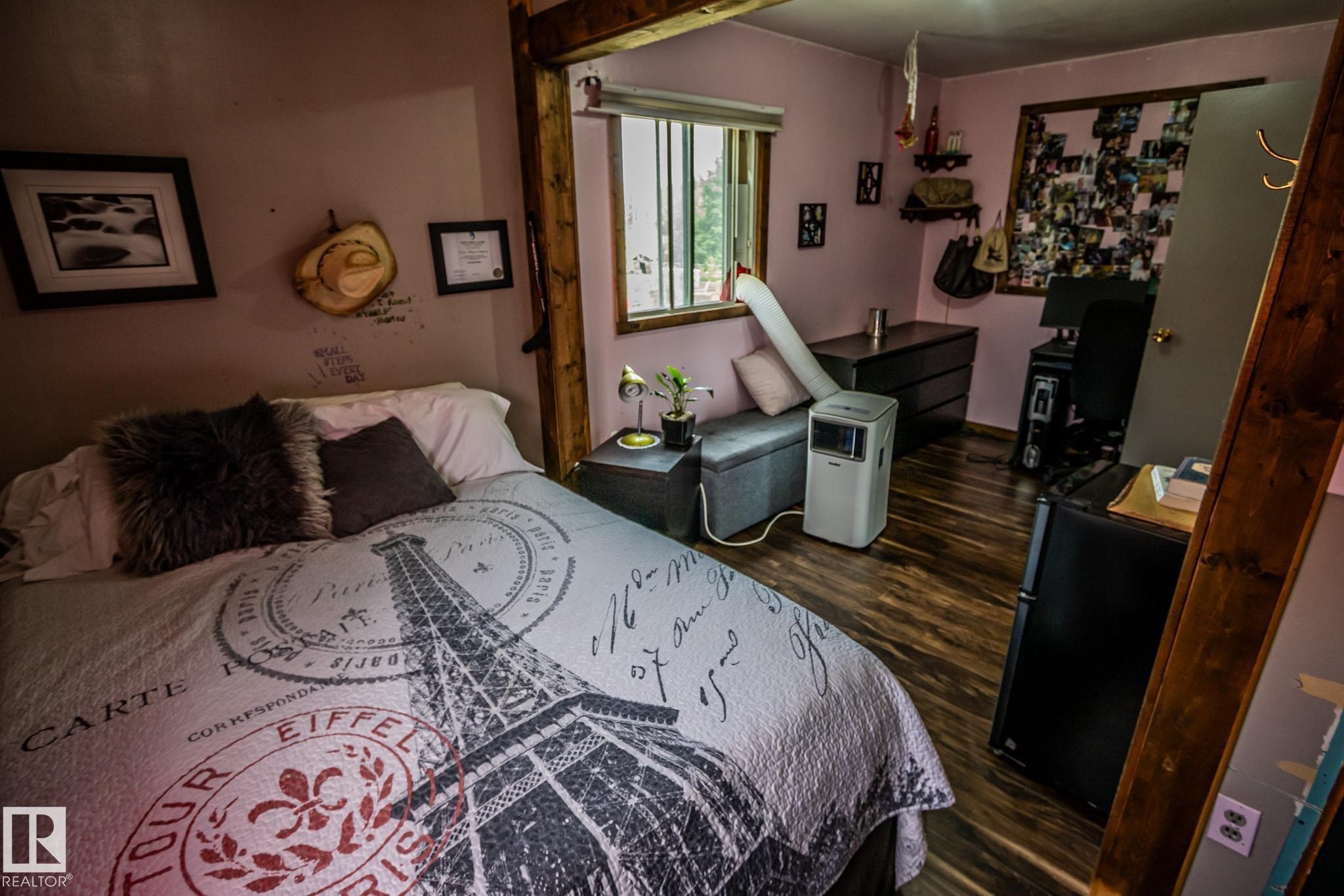 Bedroom featuring a wood post bed frame, wood-finish flooring, and soft mauve wall paint - 11218 Twp Rd 590, Rural St. Paul County, AB - Indoor Photo Showing Bedroom