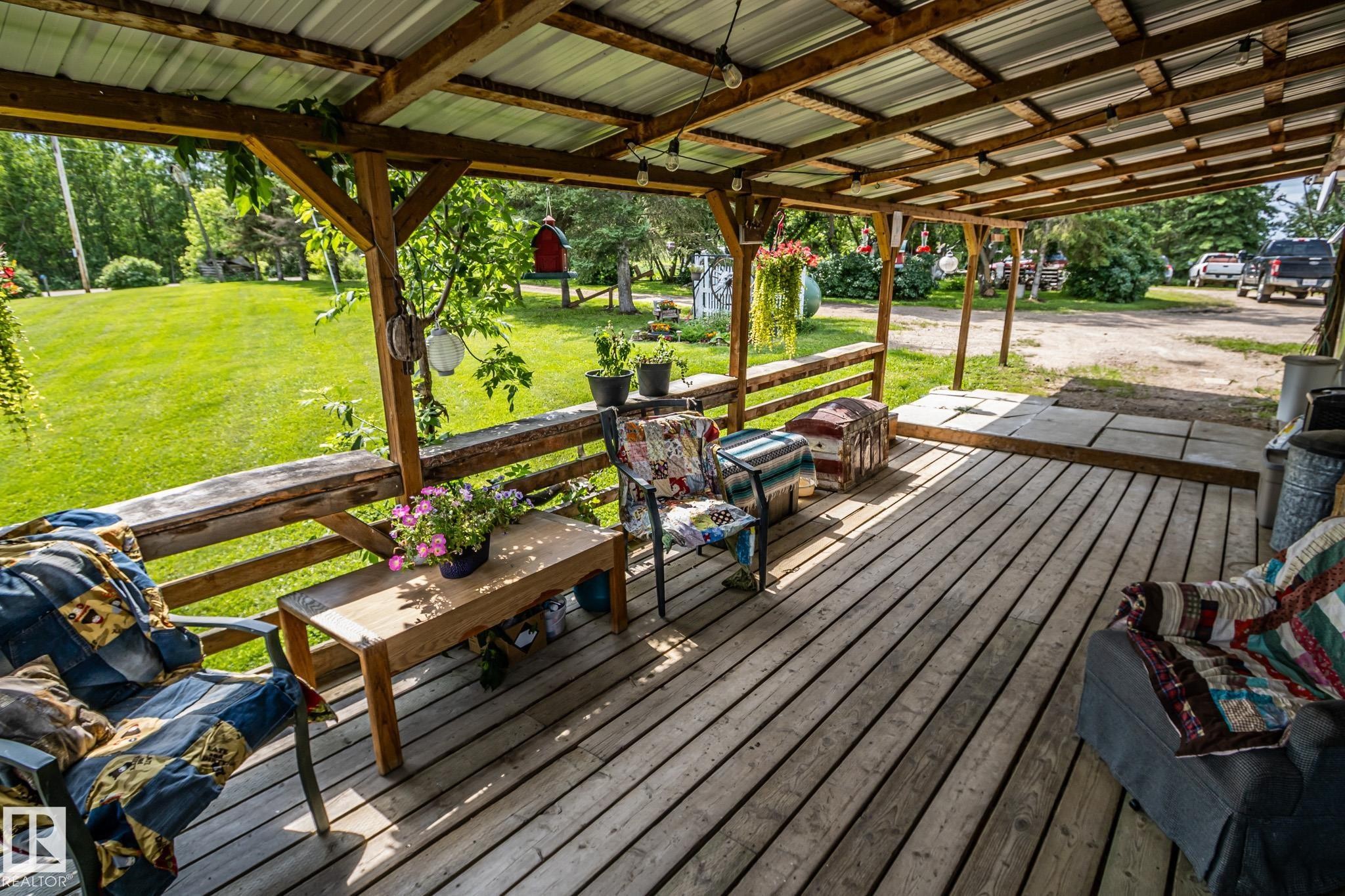 Expansive covered porch featuring wood-finish decking, exposed wood beam framing, and a corrugated metal roof - 11218 Twp Rd 590, Rural St. Paul County, AB - Outdoor With Deck Patio Veranda With Exterior