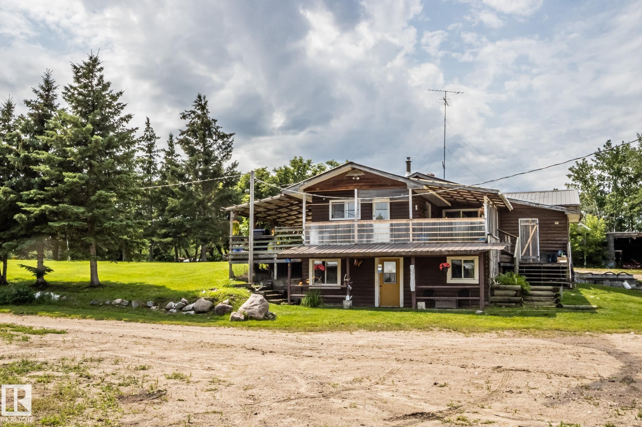 Wood-sided residence featuring an upper-level balcony with white railings, a covered lower-level porch, and a metal roof - 11218 Twp Rd 590, Rural St. Paul County, AB - Outdoor