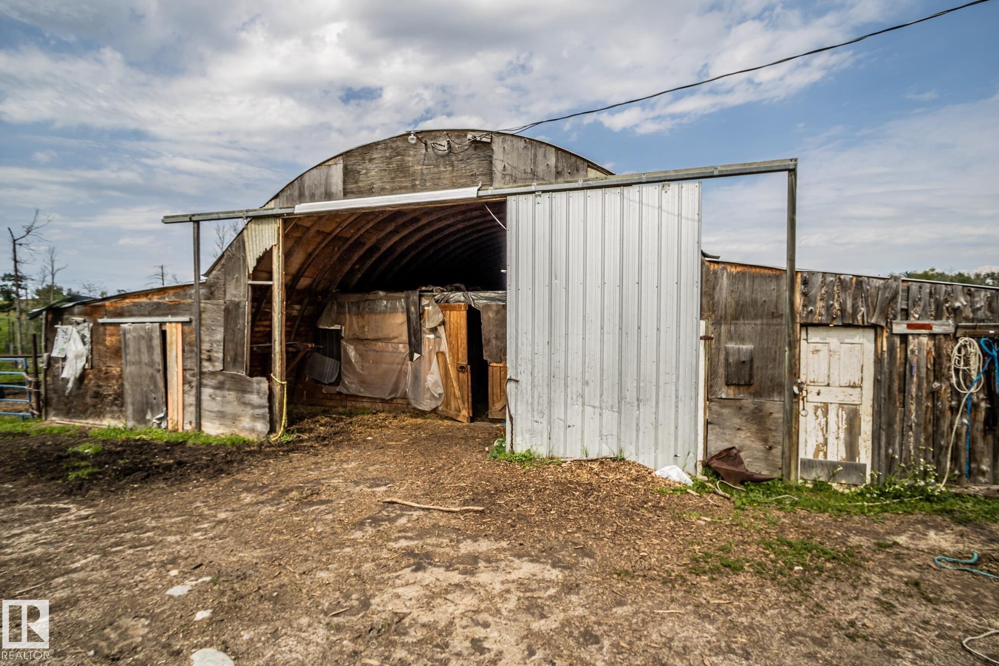 Quonset hut structure featuring a corrugated metal sliding door, exterior wooden siding, and a partial view of a metal fence - 11218 Twp Rd 590, Rural St. Paul County, AB - Outdoor