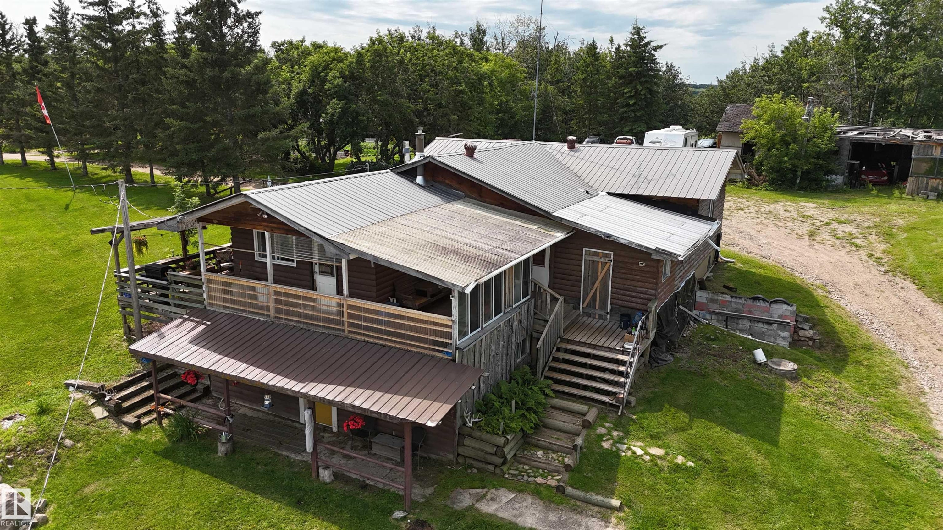 Charming residential property featuring a multi-section design with metal roofing, expansive composite decking, and covered entry porches - 11218 Twp Rd 590, Rural St. Paul County, AB - Outdoor