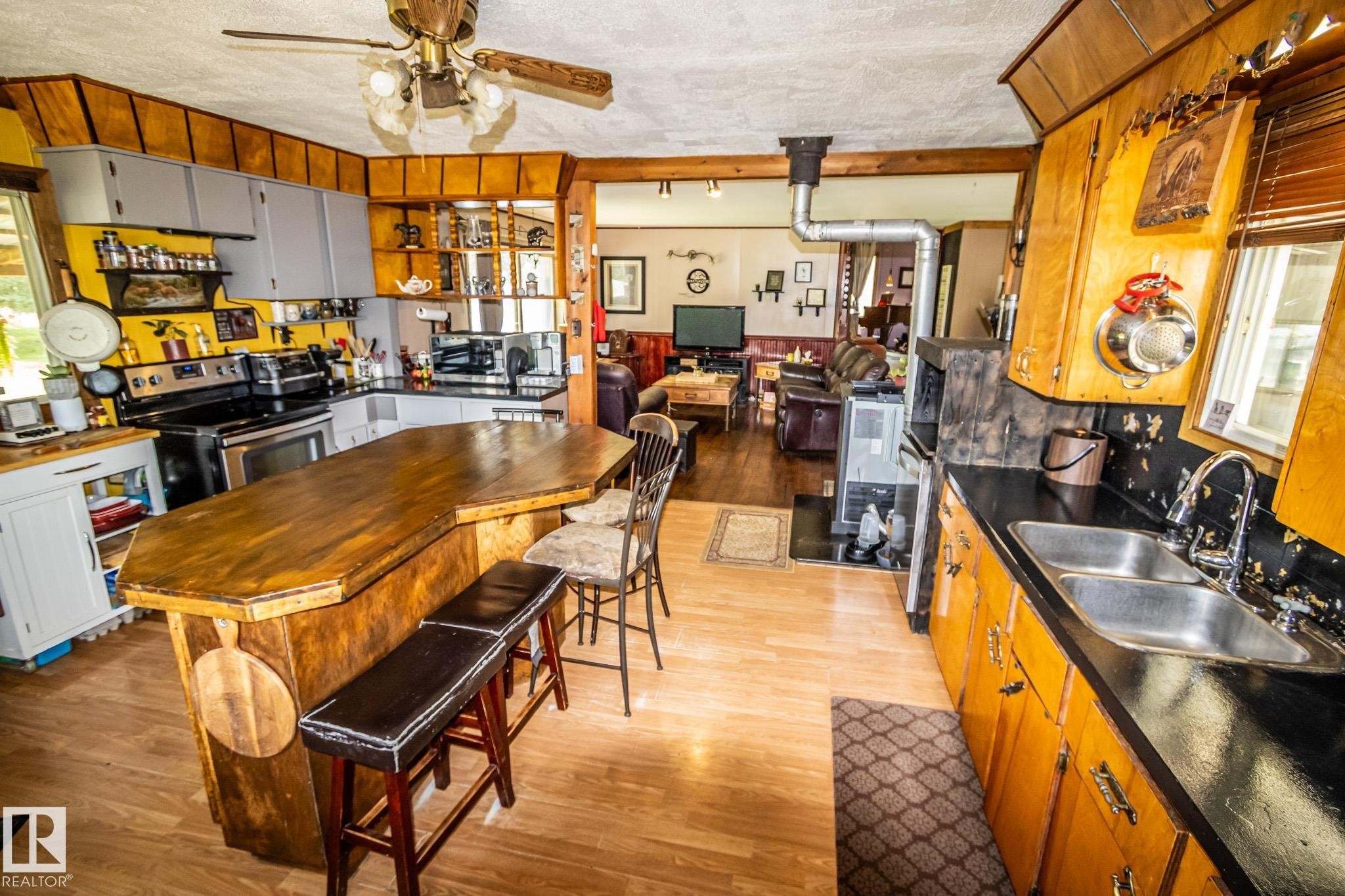 Kitchen featuring a wood-finish peninsula with seating, light wood-finish flooring, two-tone cabinetry, and a double stainless steel sink - 11218 Twp Rd 590, Rural St. Paul County, AB - Indoor