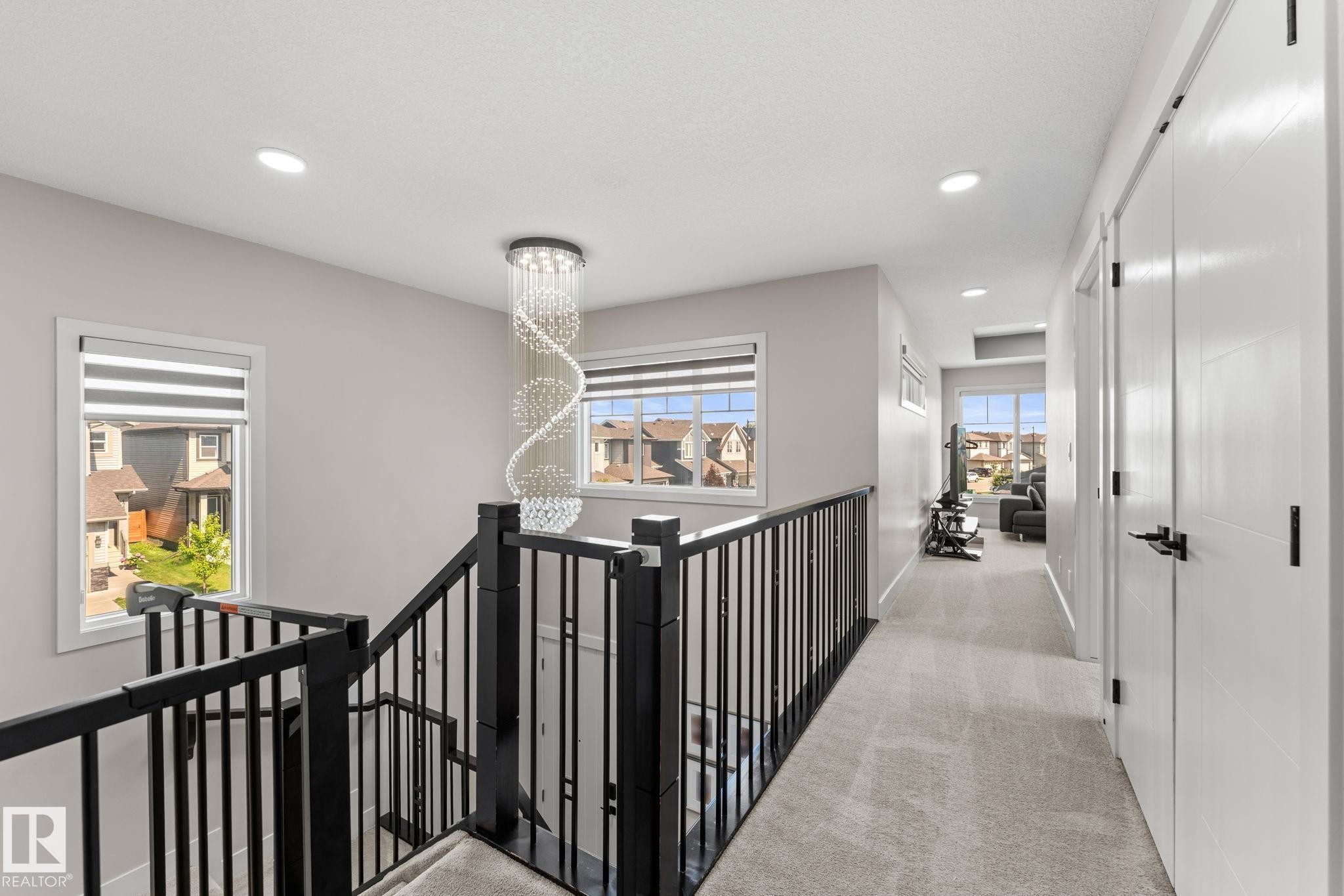 Second-floor hallway featuring black metal stair railings, recessed ceiling lighting, a decorative spiral pendant fixture, and polished concrete flooring - 12383 176 Avenue Nw, Edmonton, AB - Indoor Photo Showing Other Room