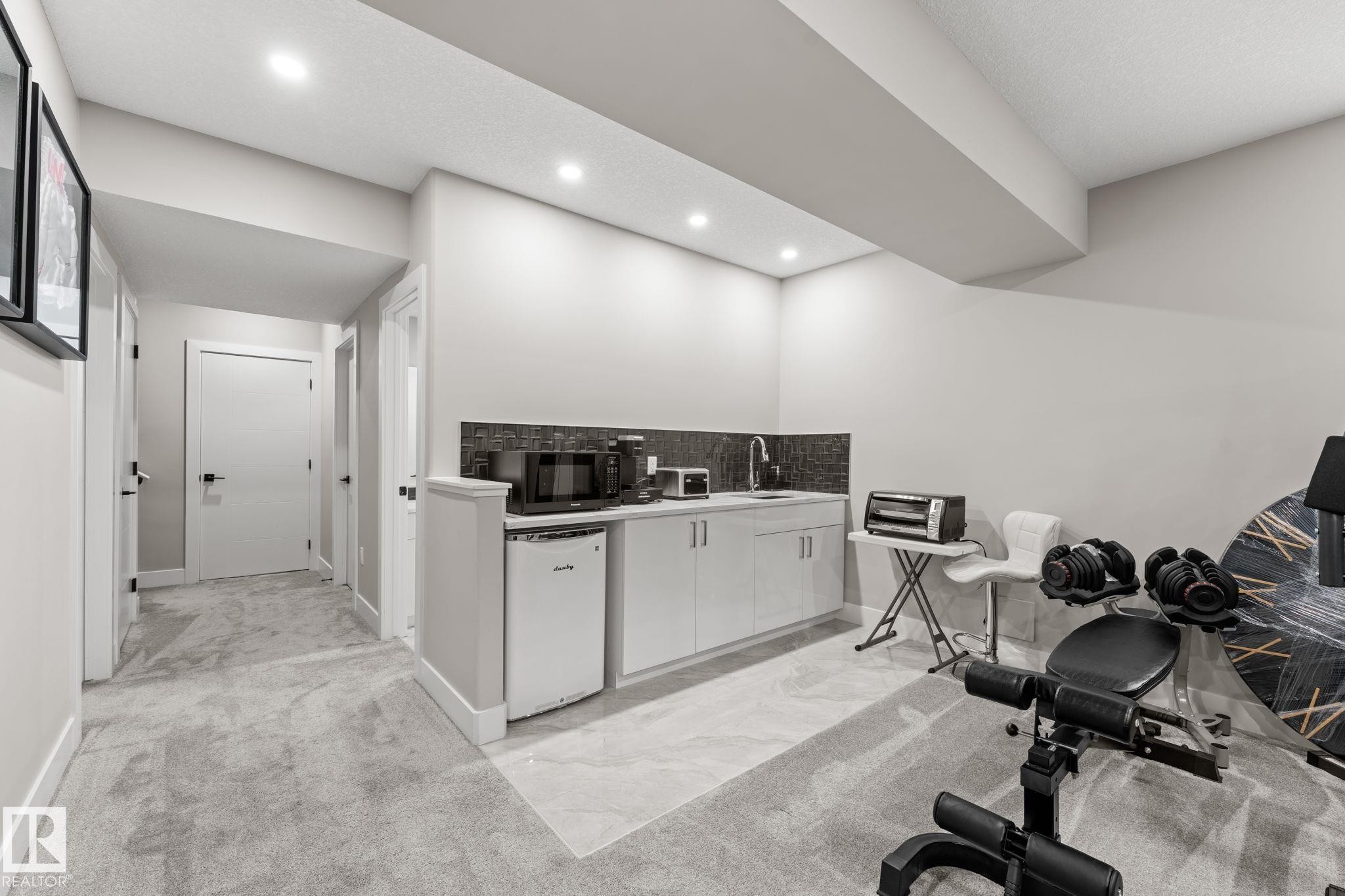 Lower level featuring a built-in kitchenette with a mini-refrigerator, sink, and dark tiled backsplash - 12383 176 Avenue Nw, Edmonton, AB - Indoor Photo Showing Gym Room