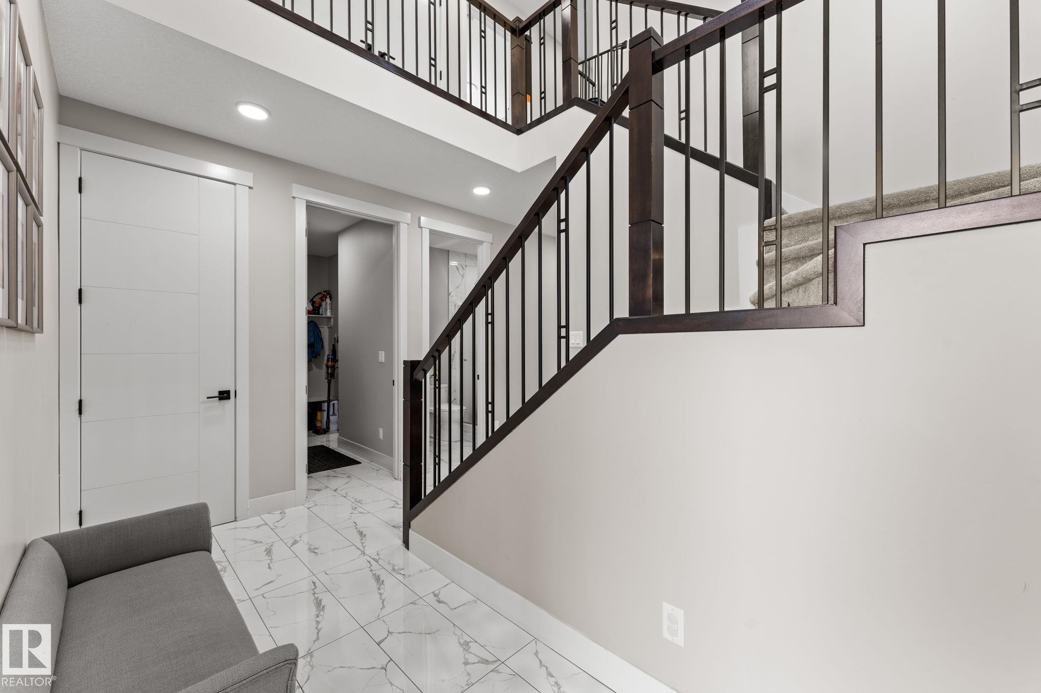 Grand entryway featuring a modern staircase with dark wood and metal railings, light gray walls, white tile flooring with veining, white panel doors, and recessed lighting - 12383 176 Avenue Nw, Edmonton, AB - Indoor