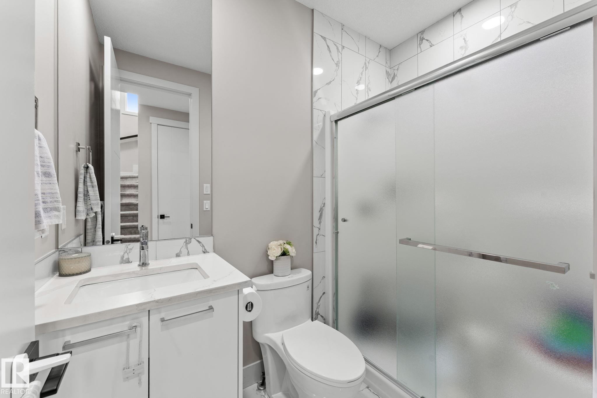 Modern bathroom featuring a floating vanity with an integrated sink and quartz countertop, chrome faucet and hardware, and a frameless glass shower enclosure with frosted panels - 12383 176 Avenue Nw, Edmonton, AB - Indoor