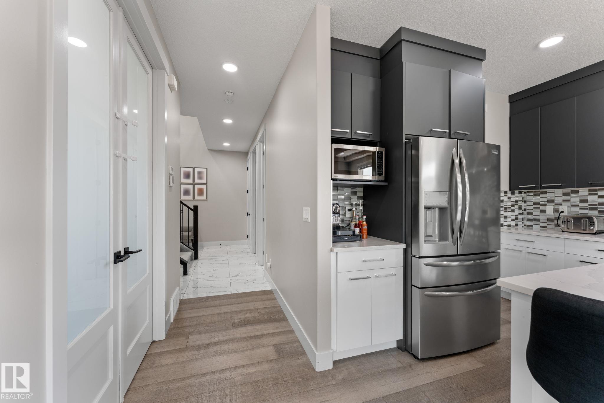 Modern kitchen featuring stainless steel appliances, dark upper cabinetry, white lower cabinetry, and a patterned tile backsplash - 12383 176 Avenue Nw, Edmonton, AB - Indoor Photo Showing Kitchen With Upgraded Kitchen