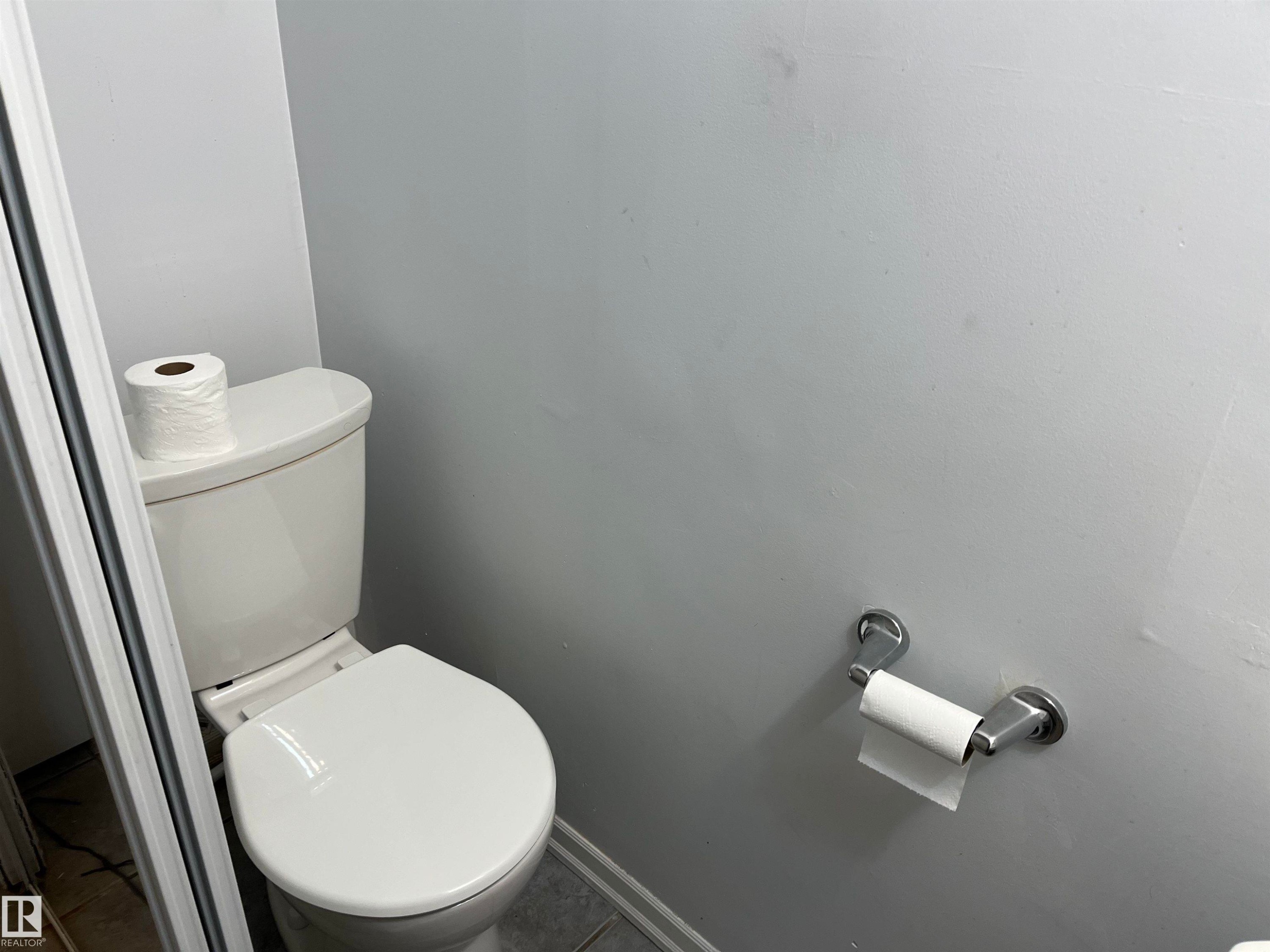 White porcelain toilet with a wall-mounted brushed metal toilet paper holder - 12011 87 Avenue Nw, Edmonton, AB - Indoor Photo Showing Bathroom