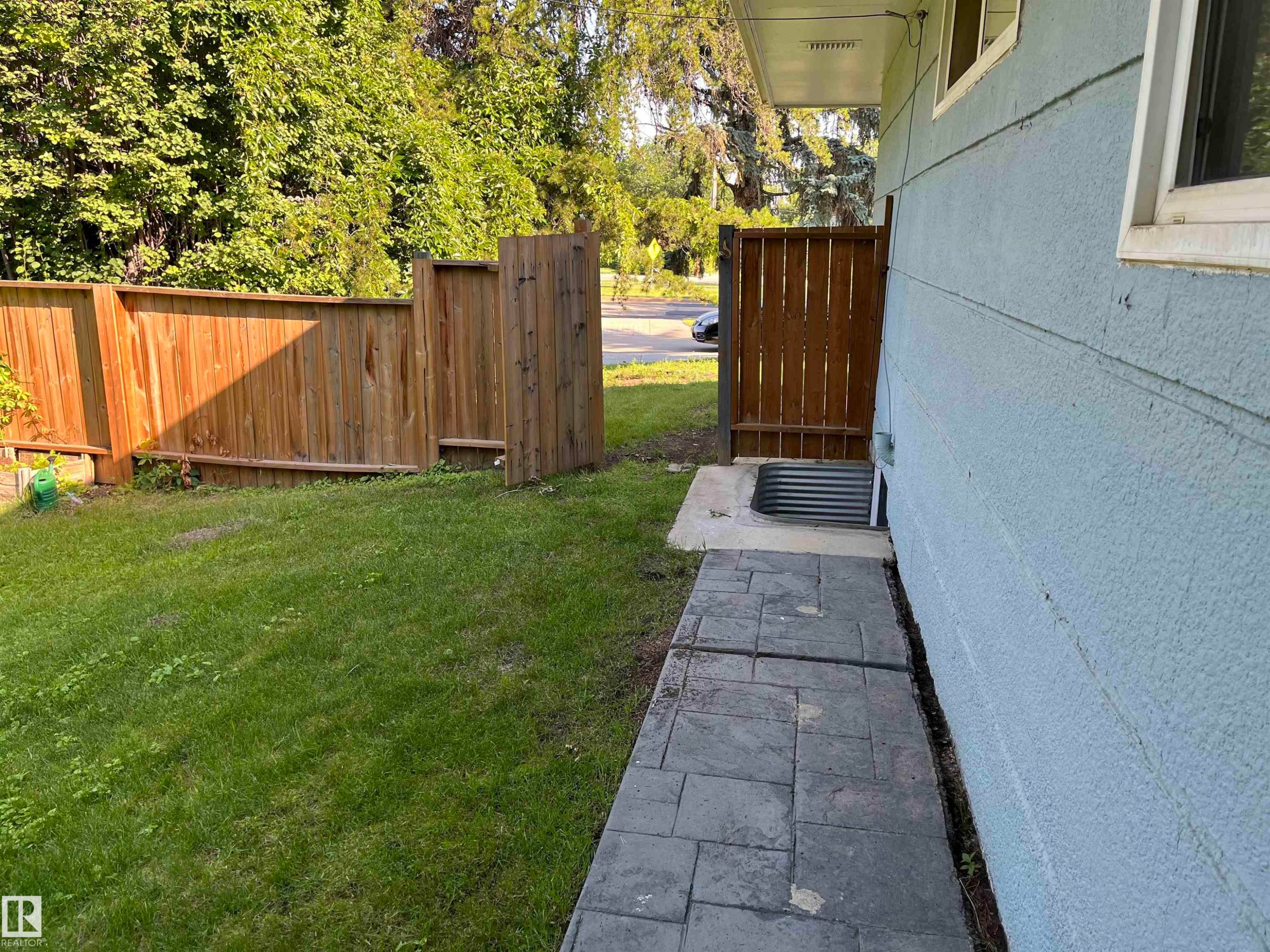 Side yard featuring a wood privacy fence, stamped concrete pathway, and a window well with a metal grate - 12011 87 Avenue Nw, Edmonton, AB - Outdoor