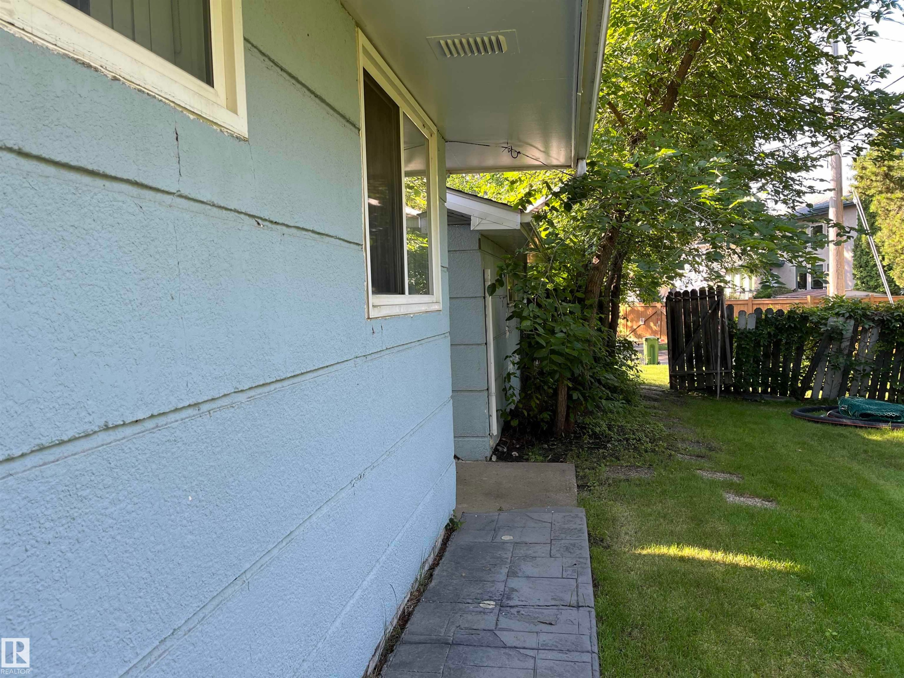 Side yard featuring a paved walkway with charcoal-toned pavers, mature landscaping with established greenery, privacy fencing, and lush lawn space - 12011 87 Avenue Nw, Edmonton, AB - Outdoor