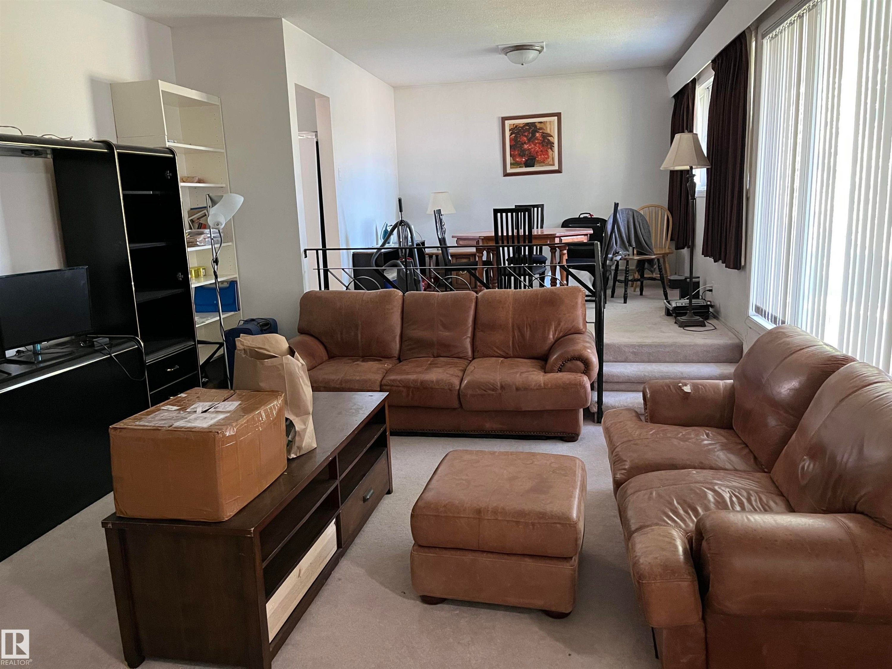 Spacious open-concept living area featuring light-colored carpeting, white walls, and a stepped transition to an elevated dining space - 12011 87 Avenue Nw, Edmonton, AB - Indoor Photo Showing Living Room
