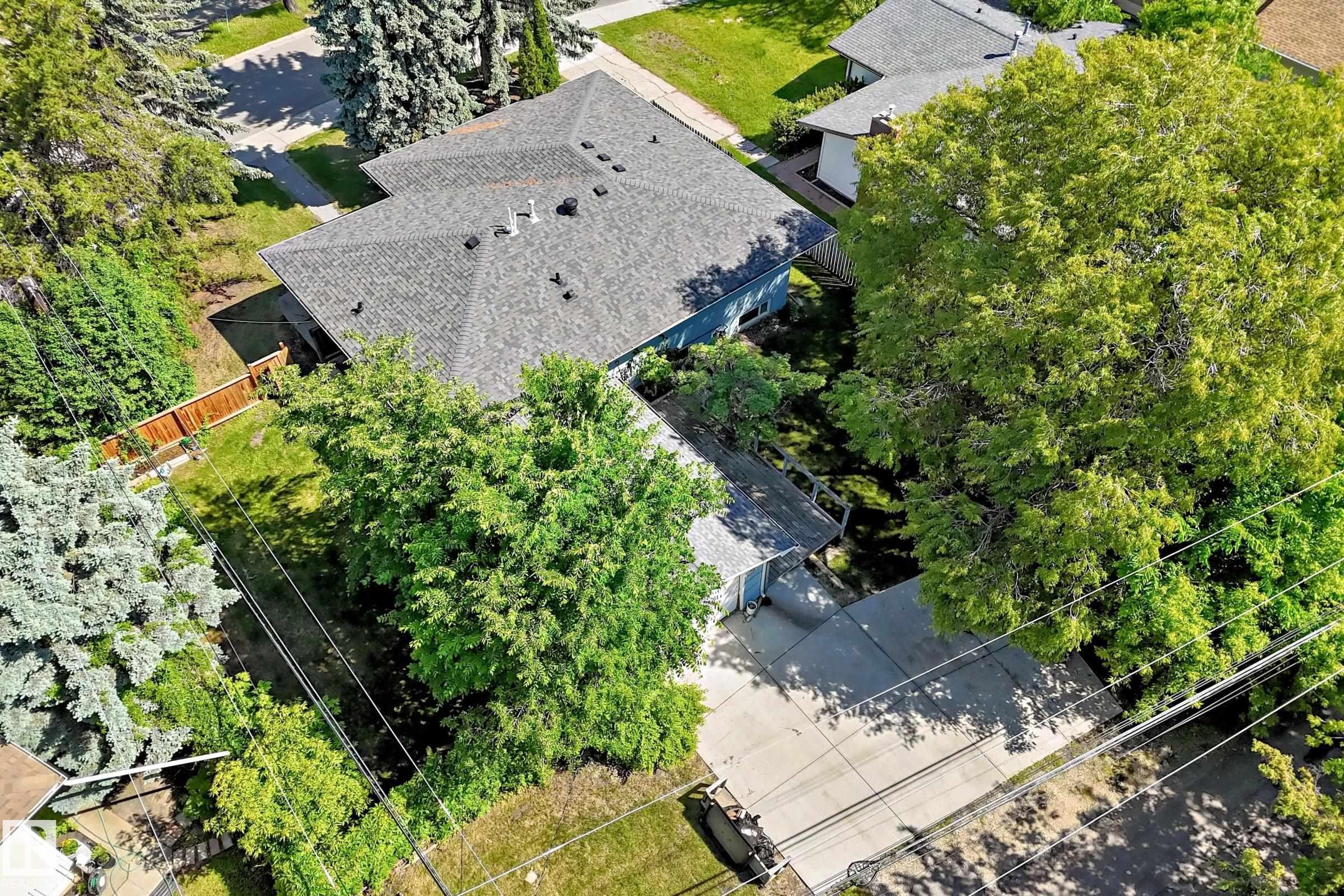Property featuring a gray shingle roof, mature landscaping, a concrete driveway, a privacy fence, and a spacious green lawn - 12011 87 Avenue Nw, Edmonton, AB - Outdoor