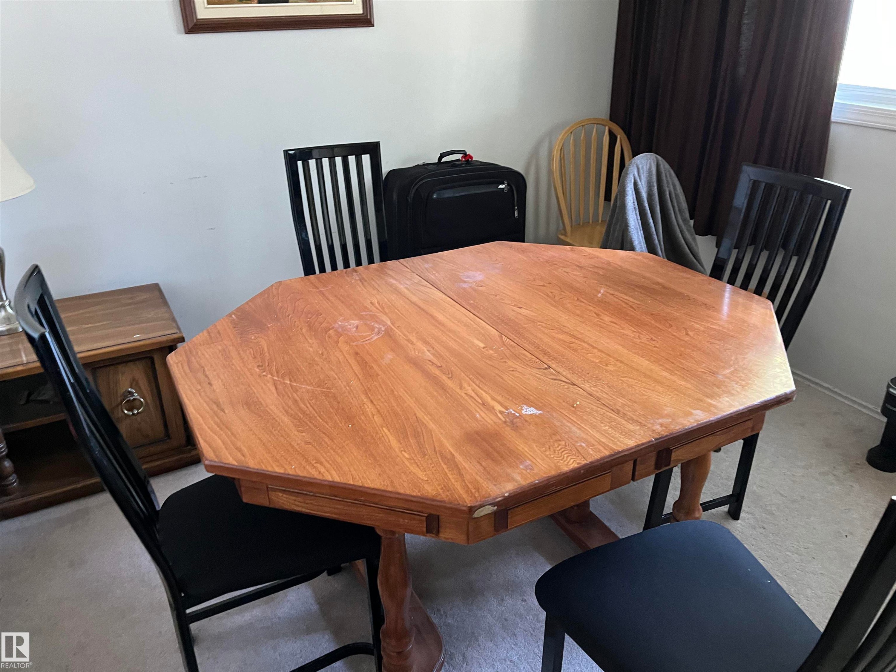 Dining room showcasing an octagonal wood-finish table with warm tonal grain, paired with black vertical-slat dining chairs featuring cushioned seats - 12011 87 Avenue Nw, Edmonton, AB - Indoor