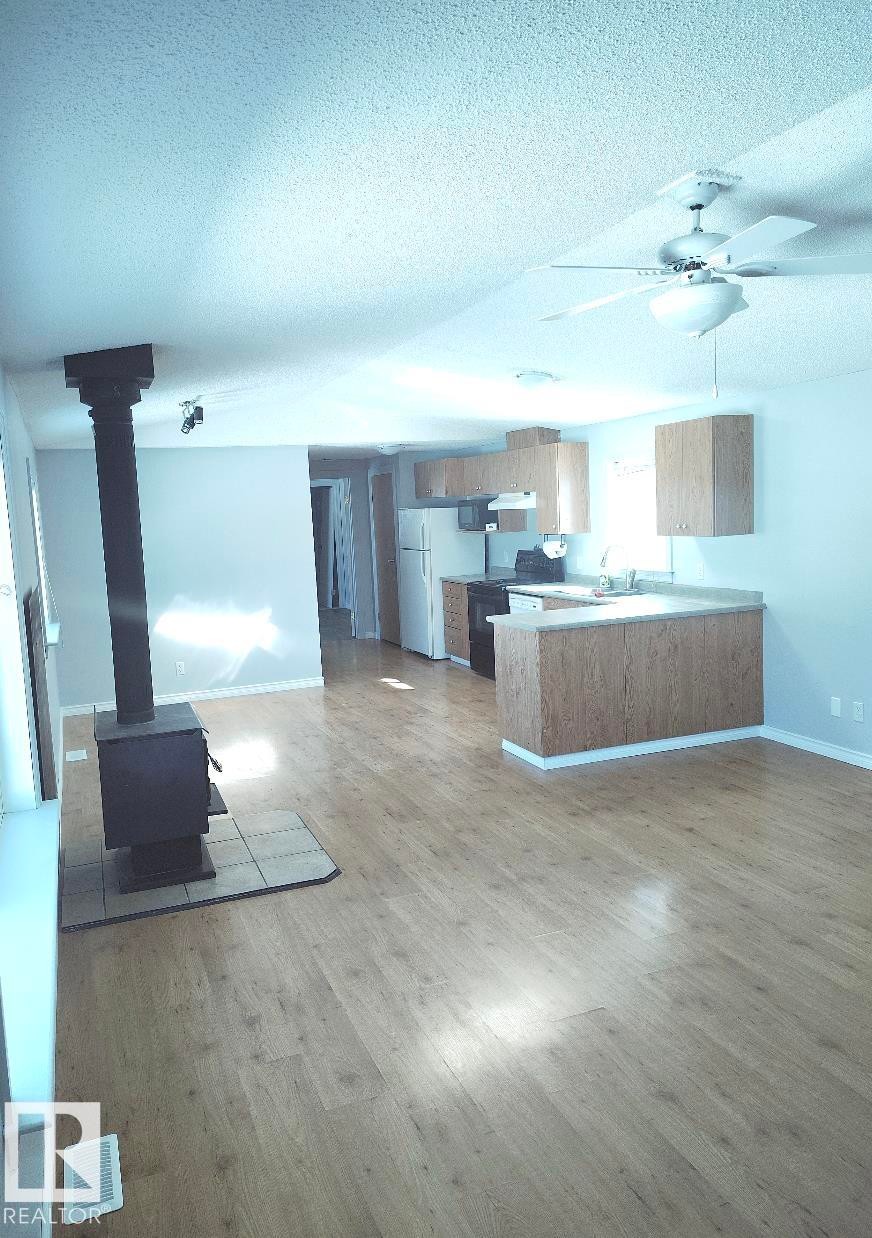Open-concept living area featuring wood-finish flooring, a freestanding wood stove with a tiled hearth, and a ceiling fan - 42 Midland Road, Millet, AB - Indoor