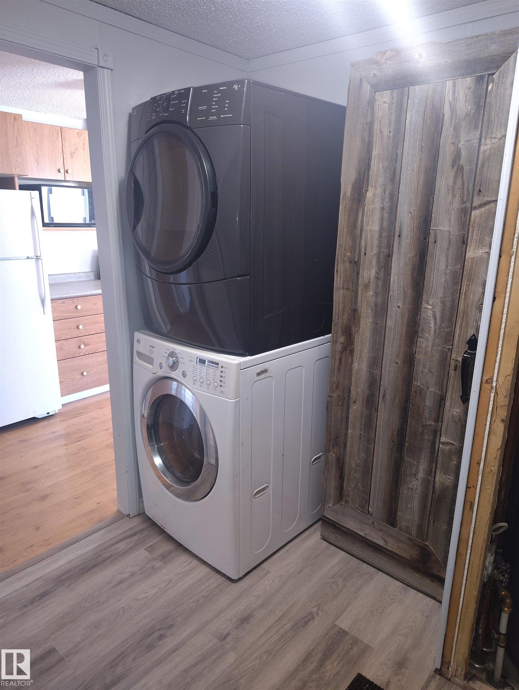 Laundry area featuring a stacked washer and dryer unit, wood-finish flooring, and a barn-style wooden door - 42 Midland Road, Millet, AB - Indoor Photo Showing Laundry Room