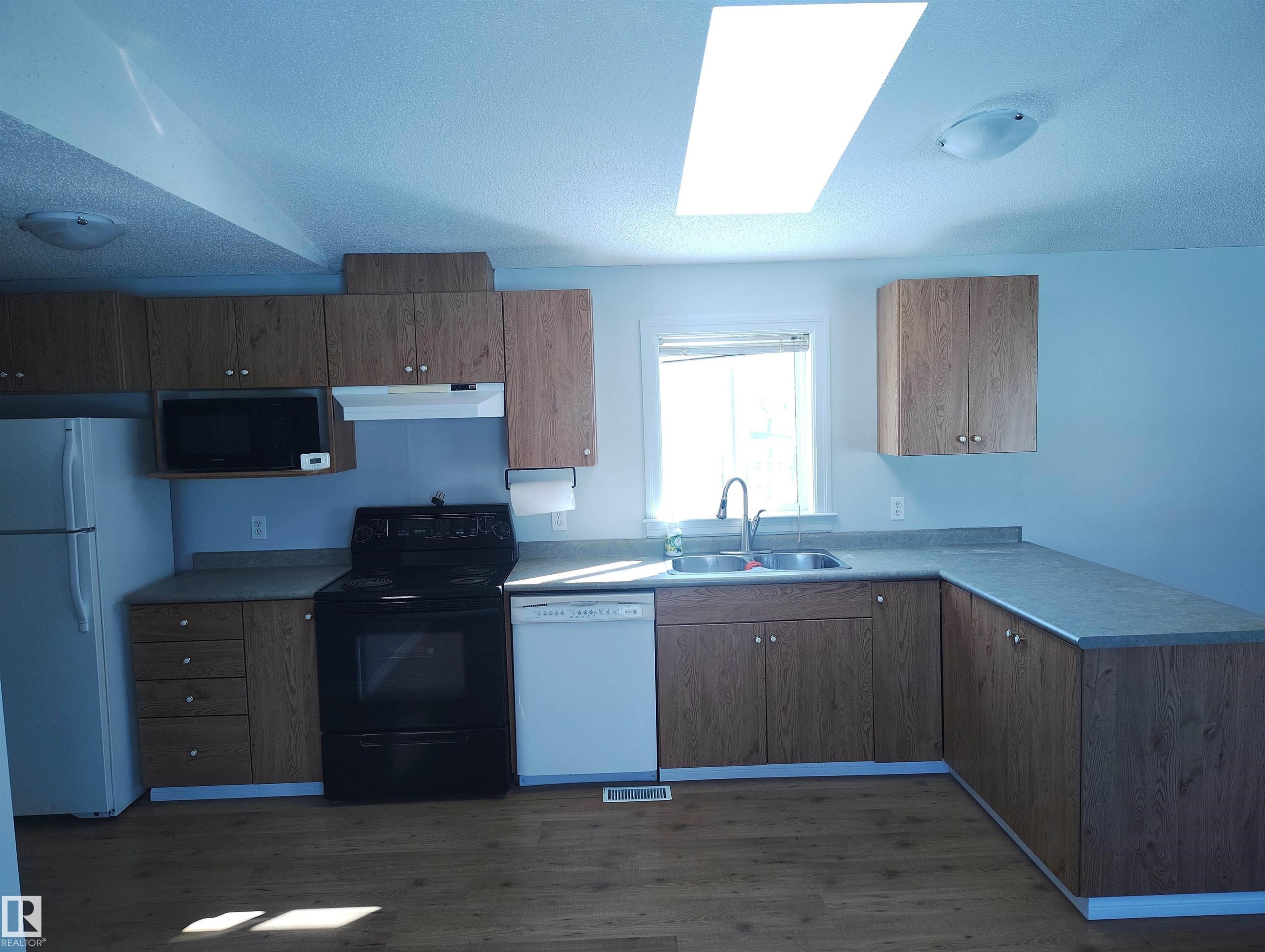 Kitchen featuring wood-finish cabinetry, a double basin stainless steel sink, a black electric range, a white dishwasher, and wood-finish flooring - 42 Midland Road, Millet, AB - Indoor Photo Showing Kitchen With Double Sink