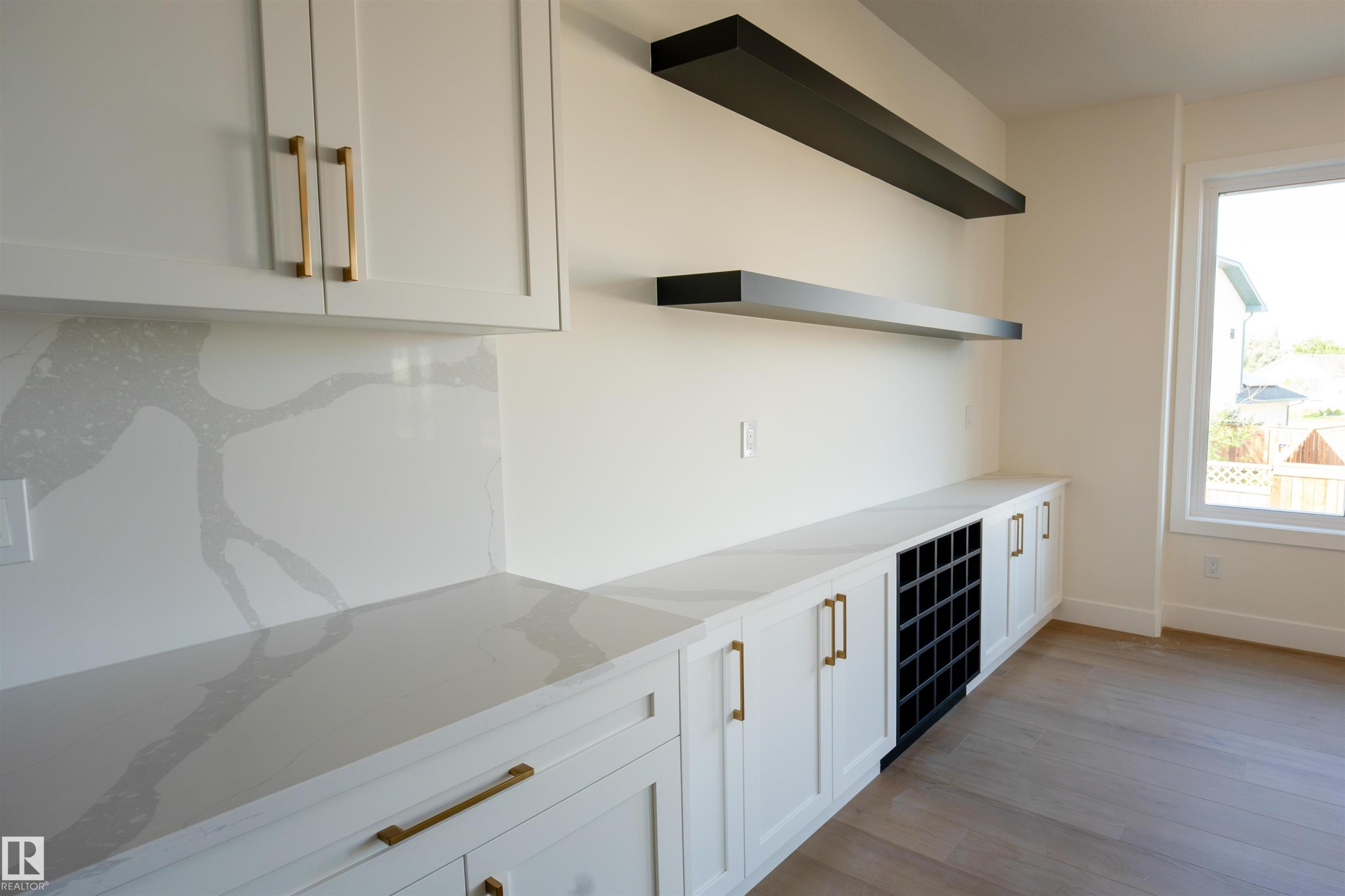 Built-in cabinetry with gold-finish hardware, light-toned countertops with distinctive veining, a dedicated wine rack, and complementary floating shelves - 34 Mckenzie Close Close, Leduc, AB - Indoor