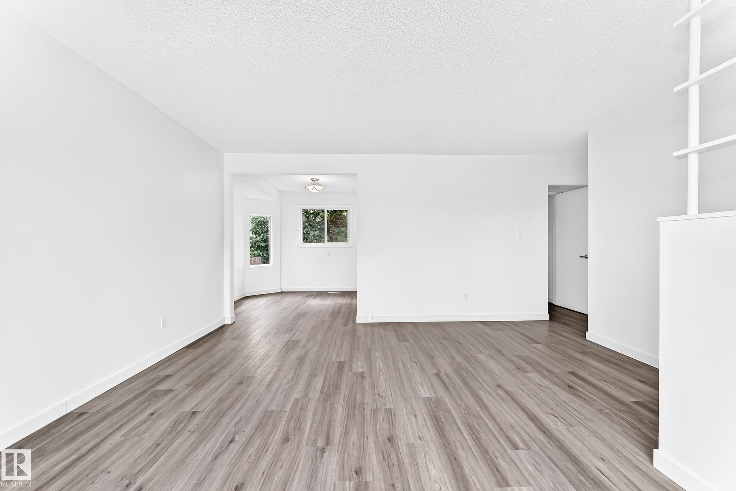 Spacious room featuring wood-finish flooring, white baseboards, and a built-in shelving unit - 5519 142 Avenue Nw, Edmonton, AB - Indoor Photo Showing Other Room