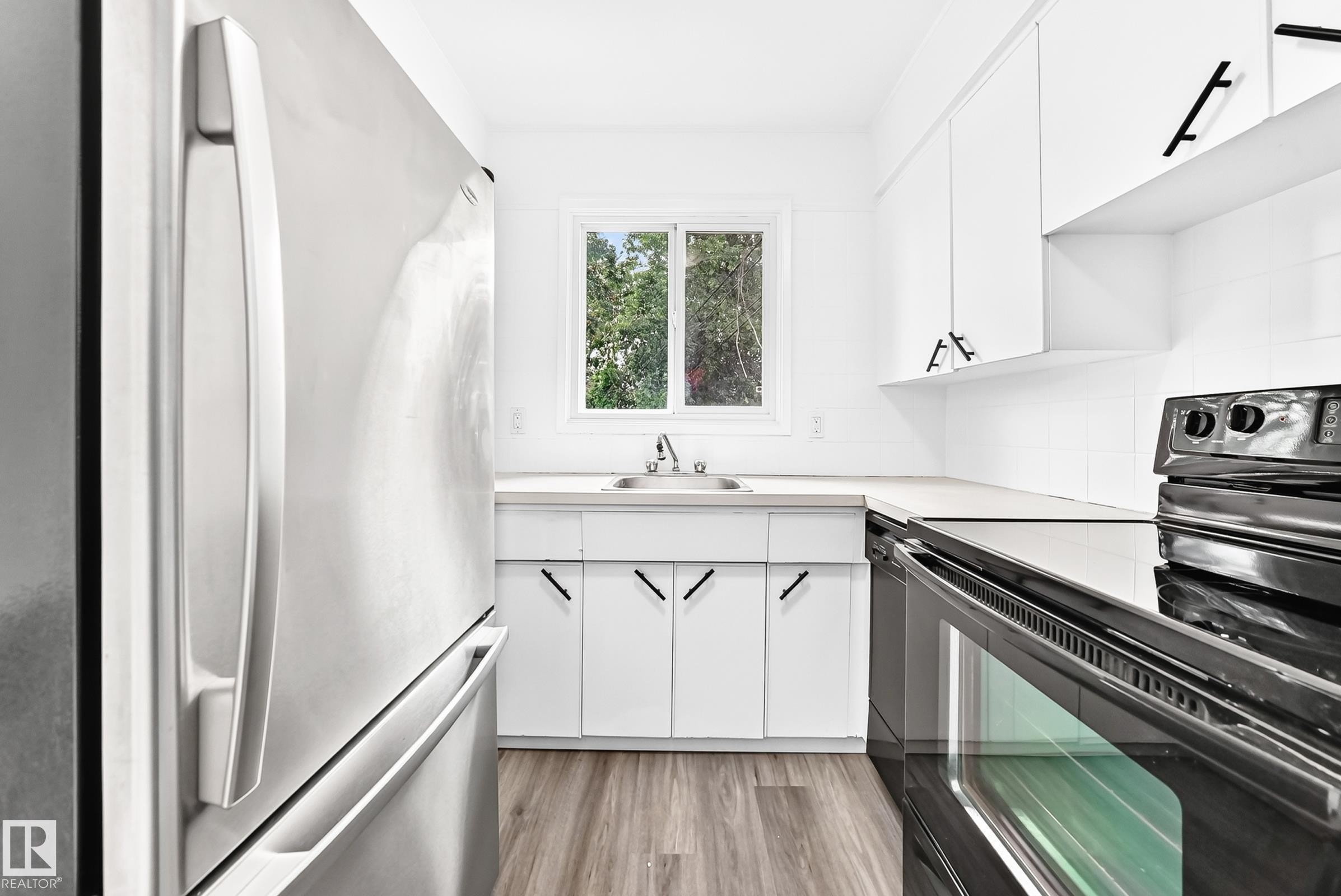 Kitchen featuring stainless steel refrigerator, white cabinetry with black hardware, black electric range, and wood-finish flooring - 5519 142 Avenue Nw, Edmonton, AB - Indoor Photo Showing Kitchen