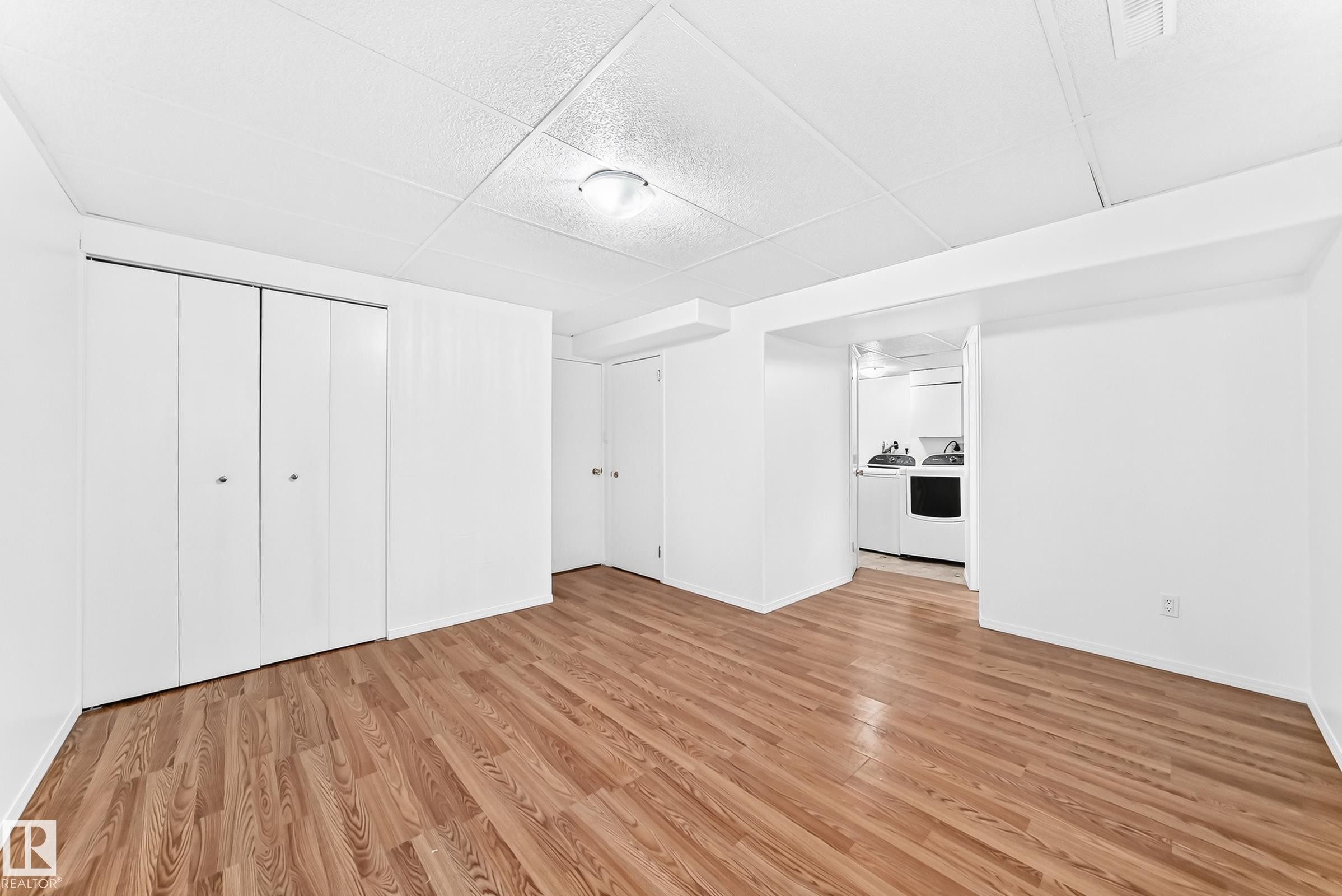 Spacious room featuring wood-finish flooring, white walls, and a drop ceiling - 5519 142 Avenue Nw, Edmonton, AB - Indoor Photo Showing Other Room