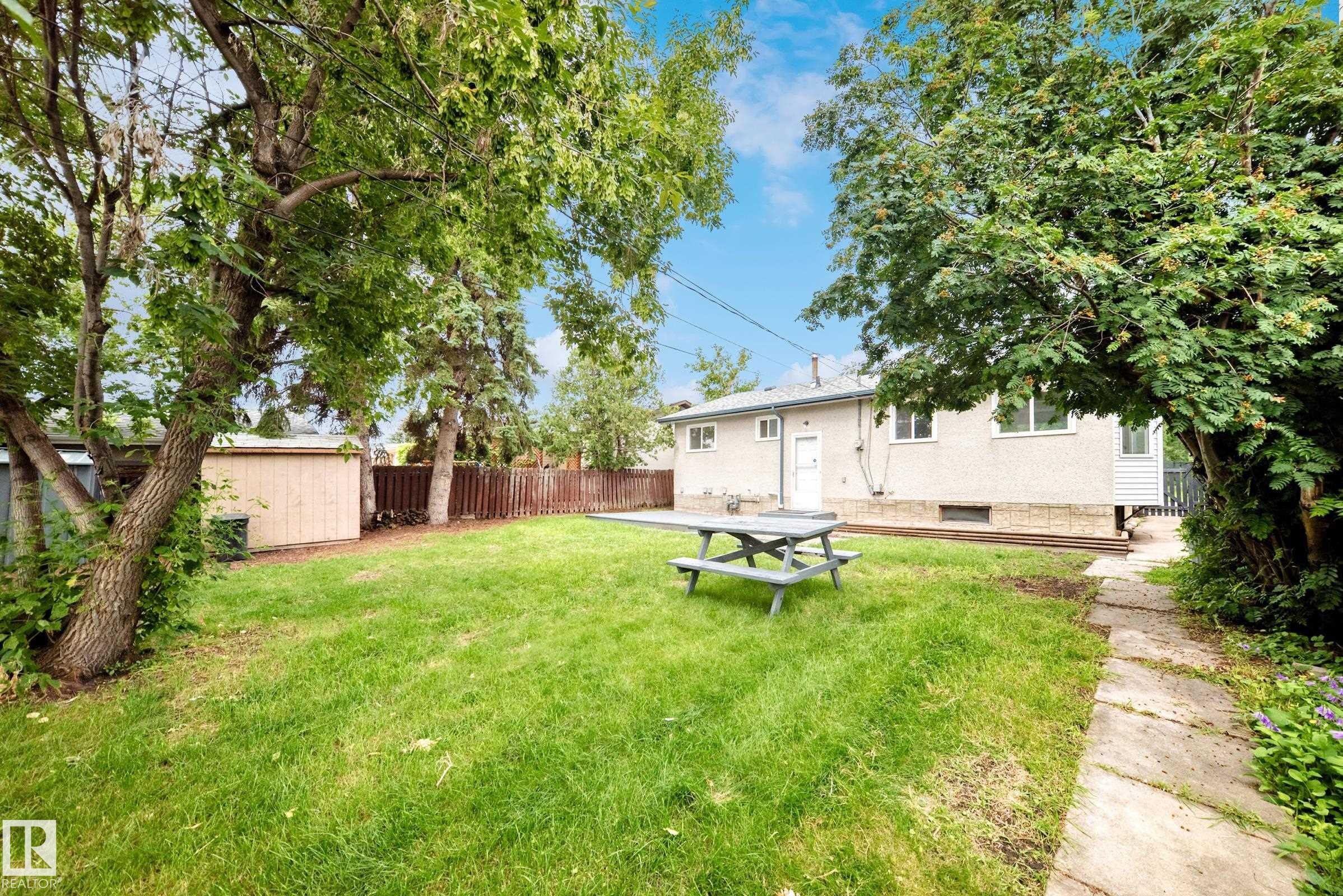 Expansive backyard featuring a manicured lawn, mature trees, and a concrete patio area - 5519 142 Avenue Nw, Edmonton, AB - Outdoor