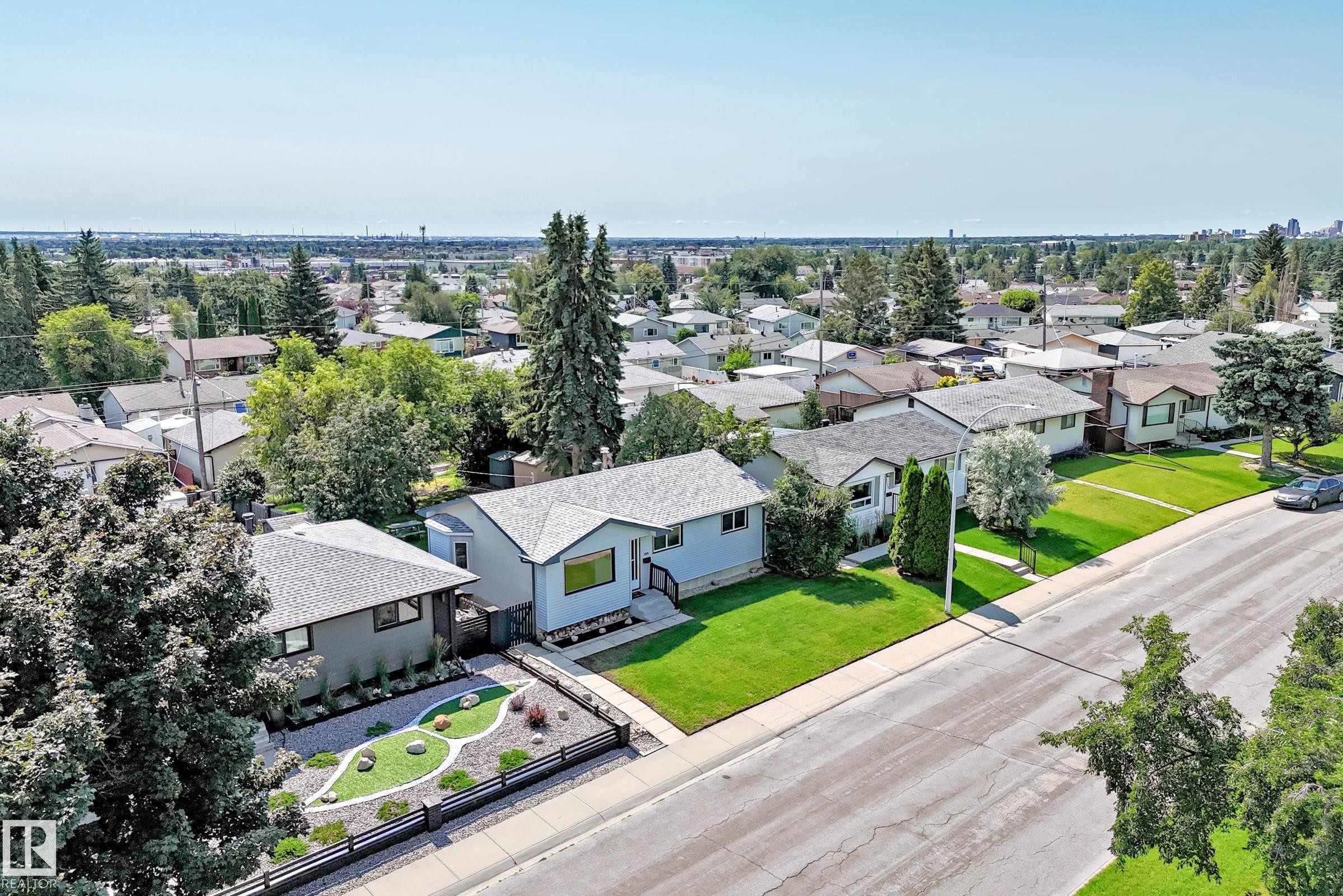 Grey-sided bungalow featuring a dark shingle roof, front landscaping with decorative stones, and a black metal fence - 5519 142 Avenue Nw, Edmonton, AB - Outdoor With View