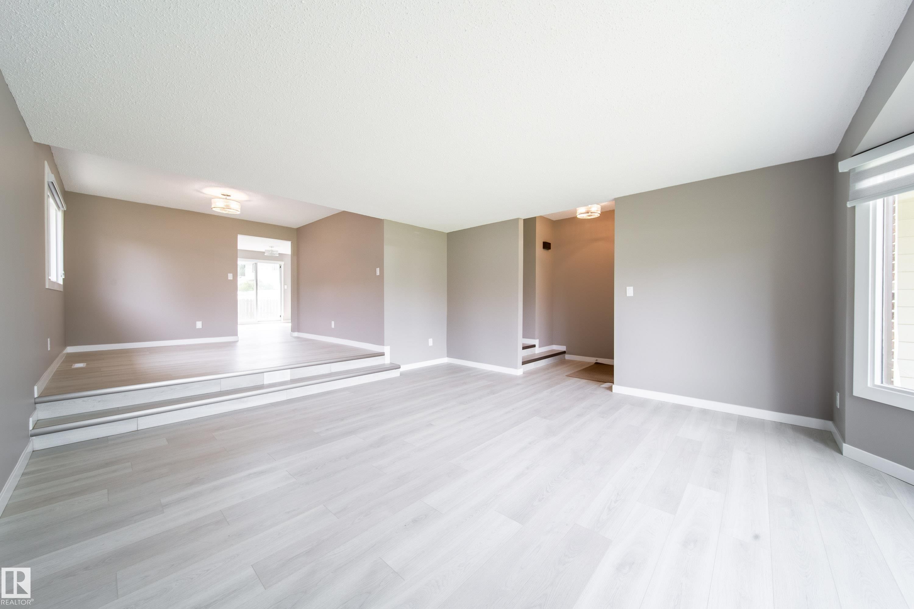 Spacious open floor plan showcasing light wood-finish flooring throughout, neutral wall finishes, and abundant natural light from multiple windows - 6907 19 Avenue Nw, Edmonton, AB - Indoor Photo Showing Other Room