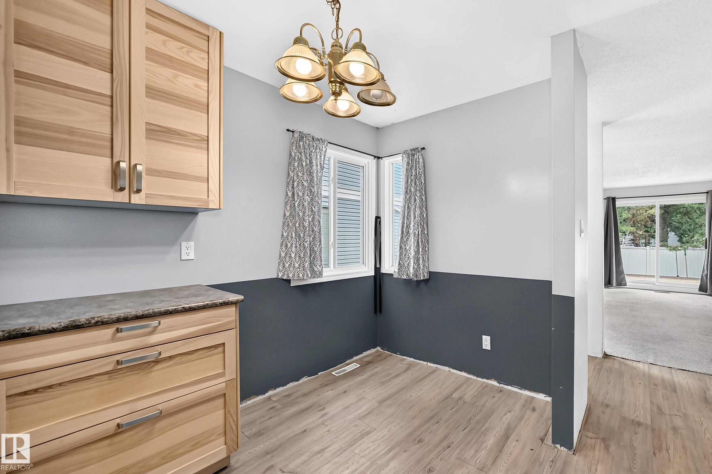 Bright kitchen and dining area featuring natural wood cabinetry with horizontal louvered doors, wood-finish flooring throughout, and a two-tone wall treatment with charcoal wainscoting - 290 Lancaster Terrace Nw, Edmonton, AB - Indoor Photo Showing Other Room
