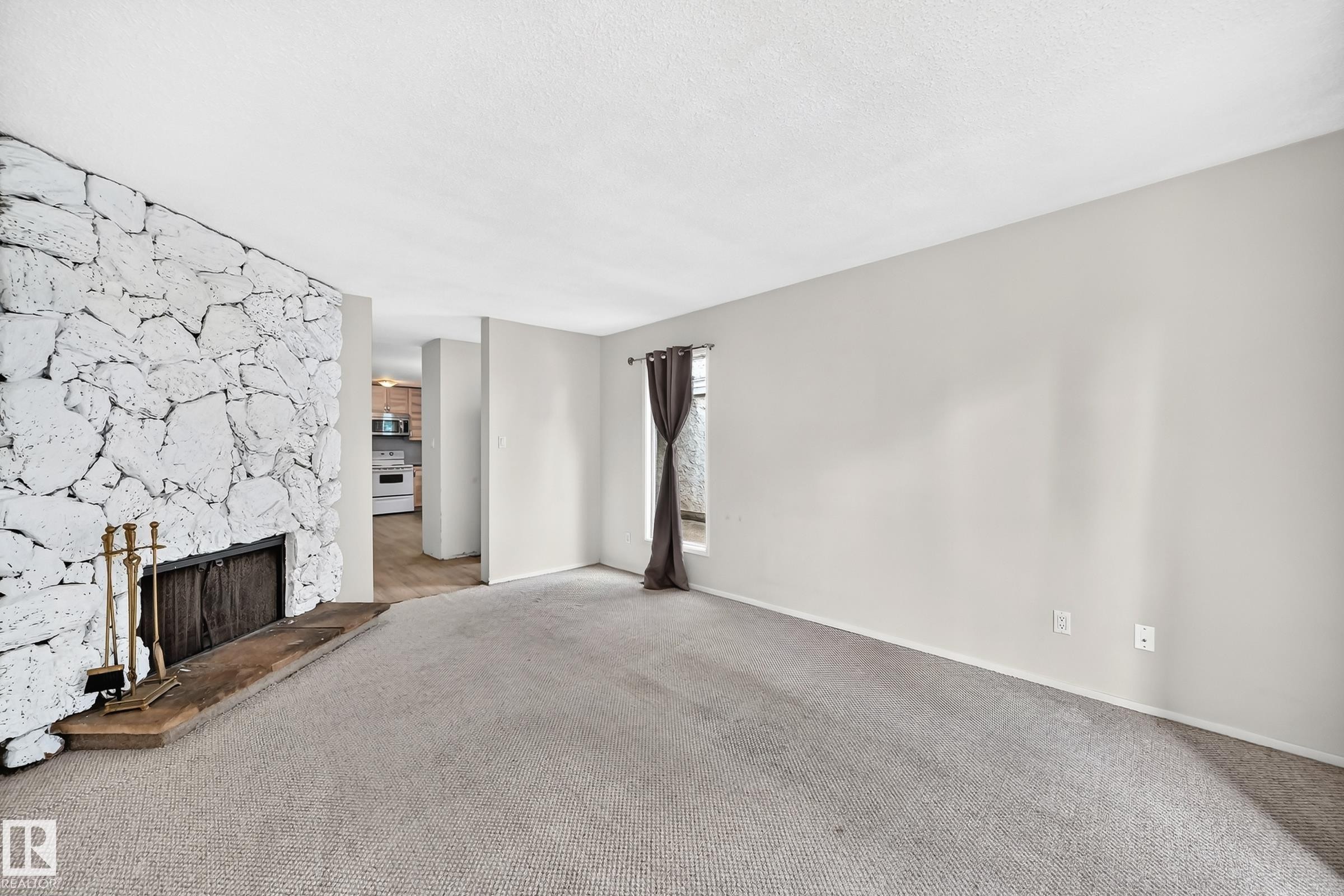 Living area featuring a stone accent wall, fireplace with hearth, and neutral carpeting - 290 Lancaster Terrace Nw, Edmonton, AB - Indoor With Fireplace