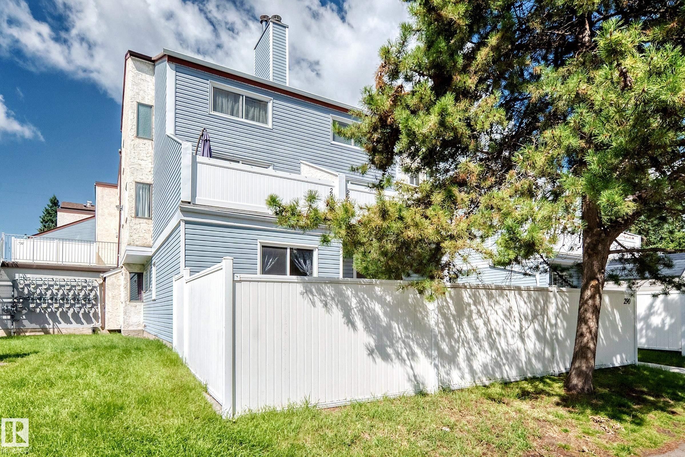 Modern multi-level residence featuring clean-lined siding exterior, white vinyl privacy fencing, mature landscaping with established trees, manicured lawn, and contemporary architectural design with multiple window placements for natural light - 290 Lancaster Terrace Nw, Edmonton, AB - Outdoor