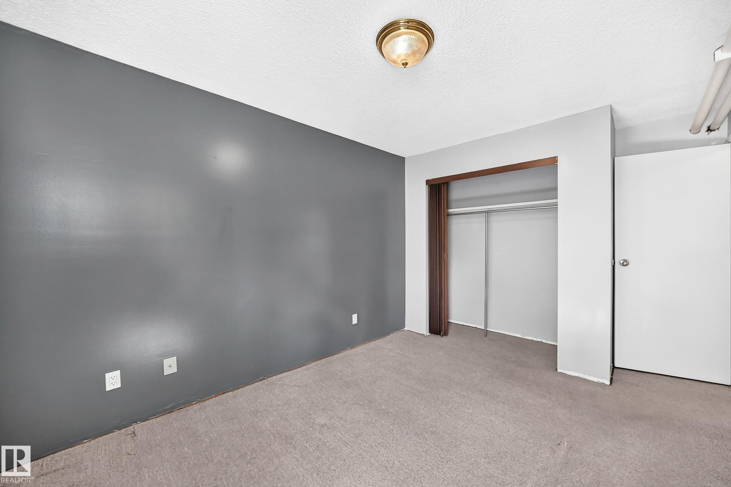 Room with textured ceiling, flush mount ceiling light fixture, gray painted wall, built-in closet with sliding doors, and light-colored carpet flooring - 290 Lancaster Terrace Nw, Edmonton, AB - Indoor Photo Showing Other Room