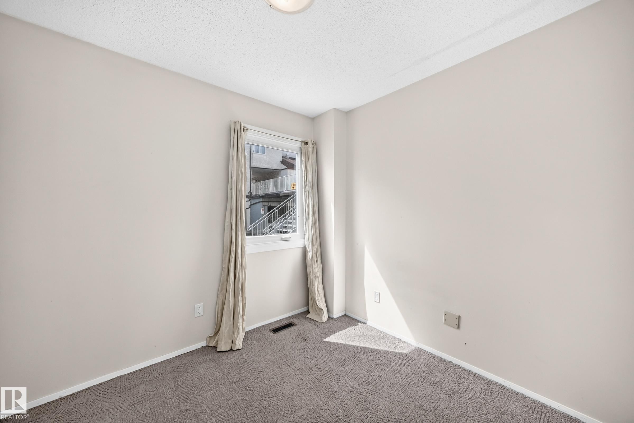 Bright corner bedroom with neutral wall finishes, neutral-tone carpeting, and natural light from a large window with curtain hardware - 290 Lancaster Terrace Nw, Edmonton, AB - Indoor Photo Showing Other Room