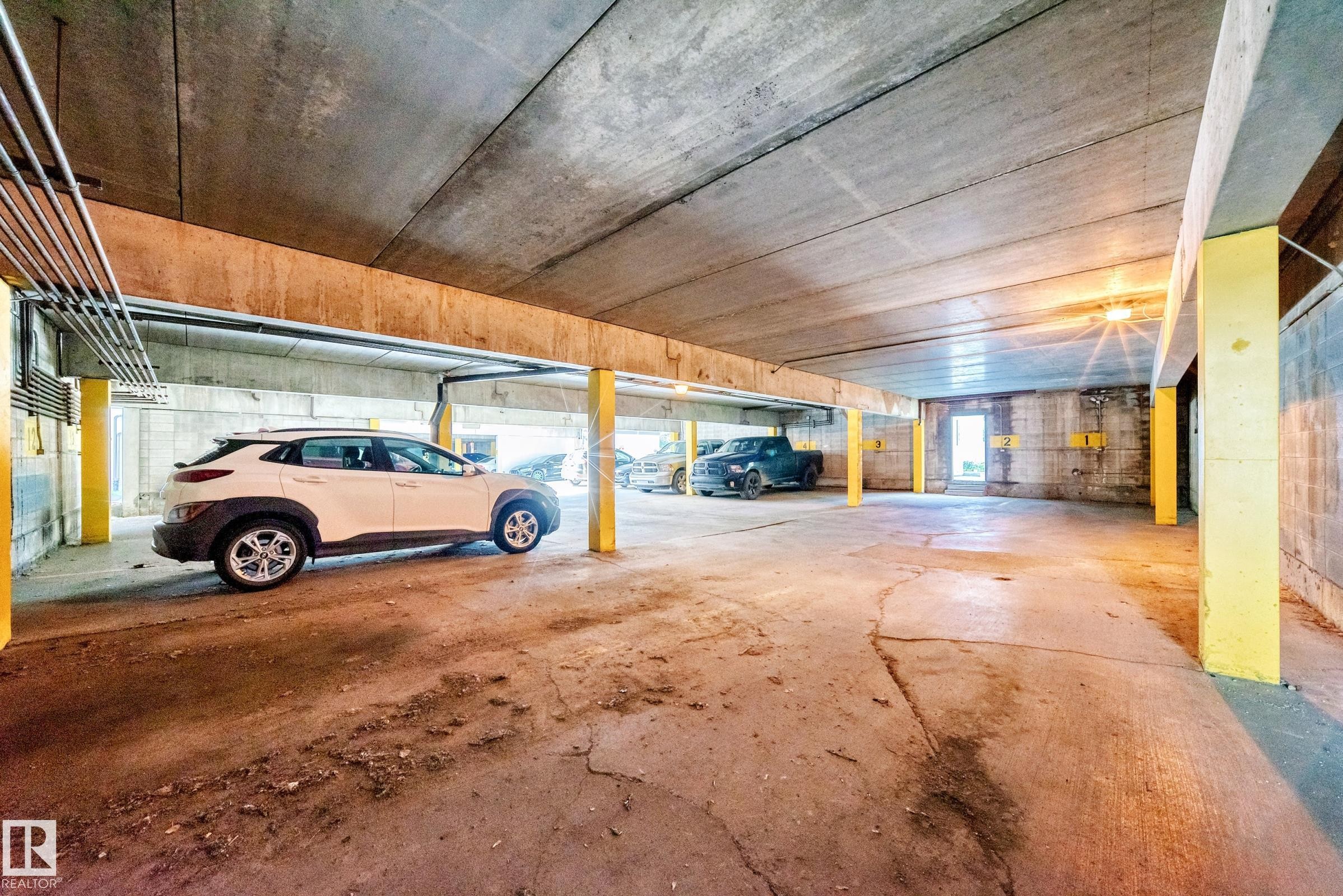 Concrete parking garage featuring exposed concrete ceilings and support beams, illuminated overhead lighting, and ample space - 290 Lancaster Terrace Nw, Edmonton, AB - Indoor Photo Showing Garage