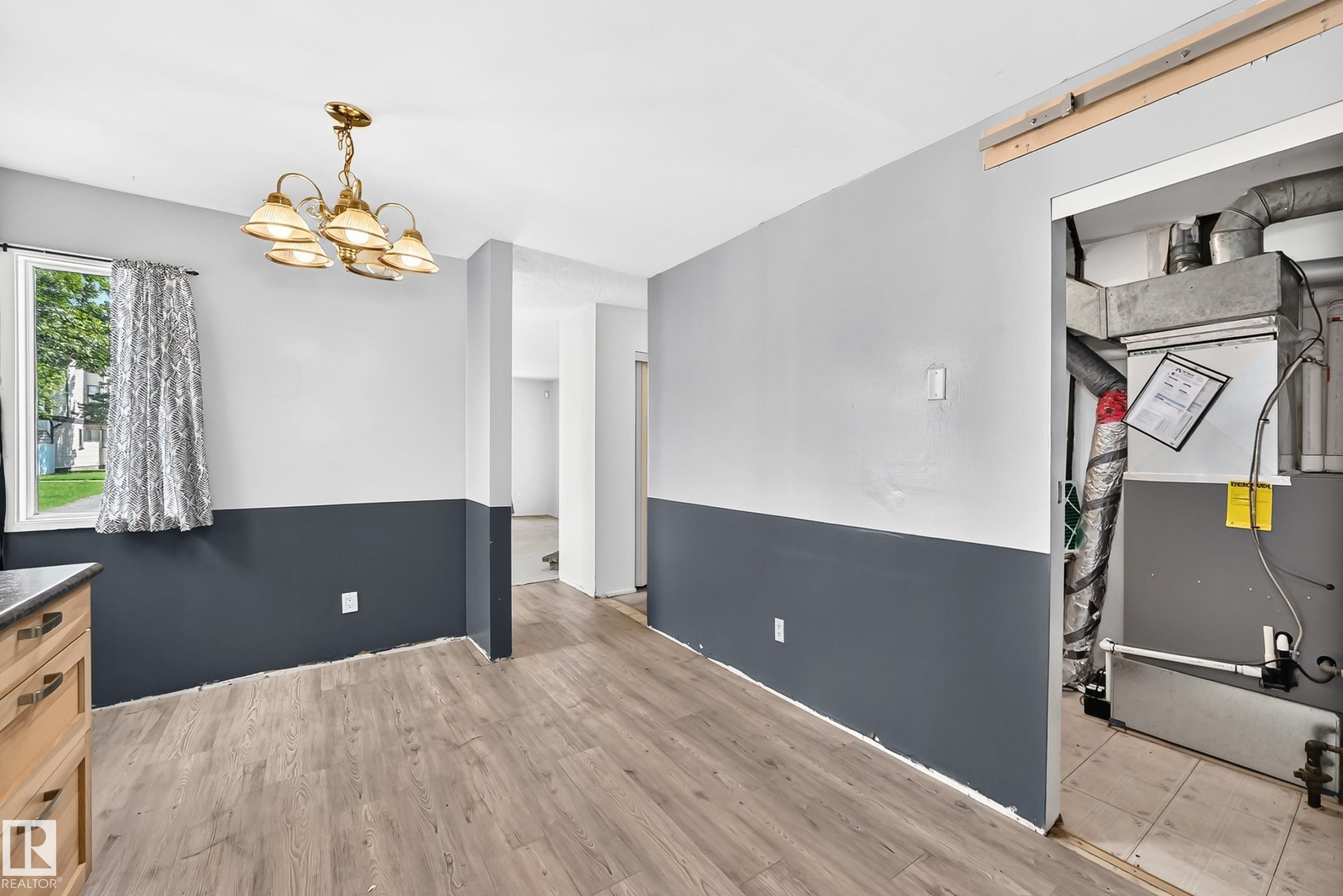 Spacious utility room featuring two-tone wall treatment with contrasting dark lower paneling and crisp white upper walls, wood-finish flooring throughout, and direct access to organized storage closet - 290 Lancaster Terrace Nw, Edmonton, AB - Indoor Photo Showing Other Room