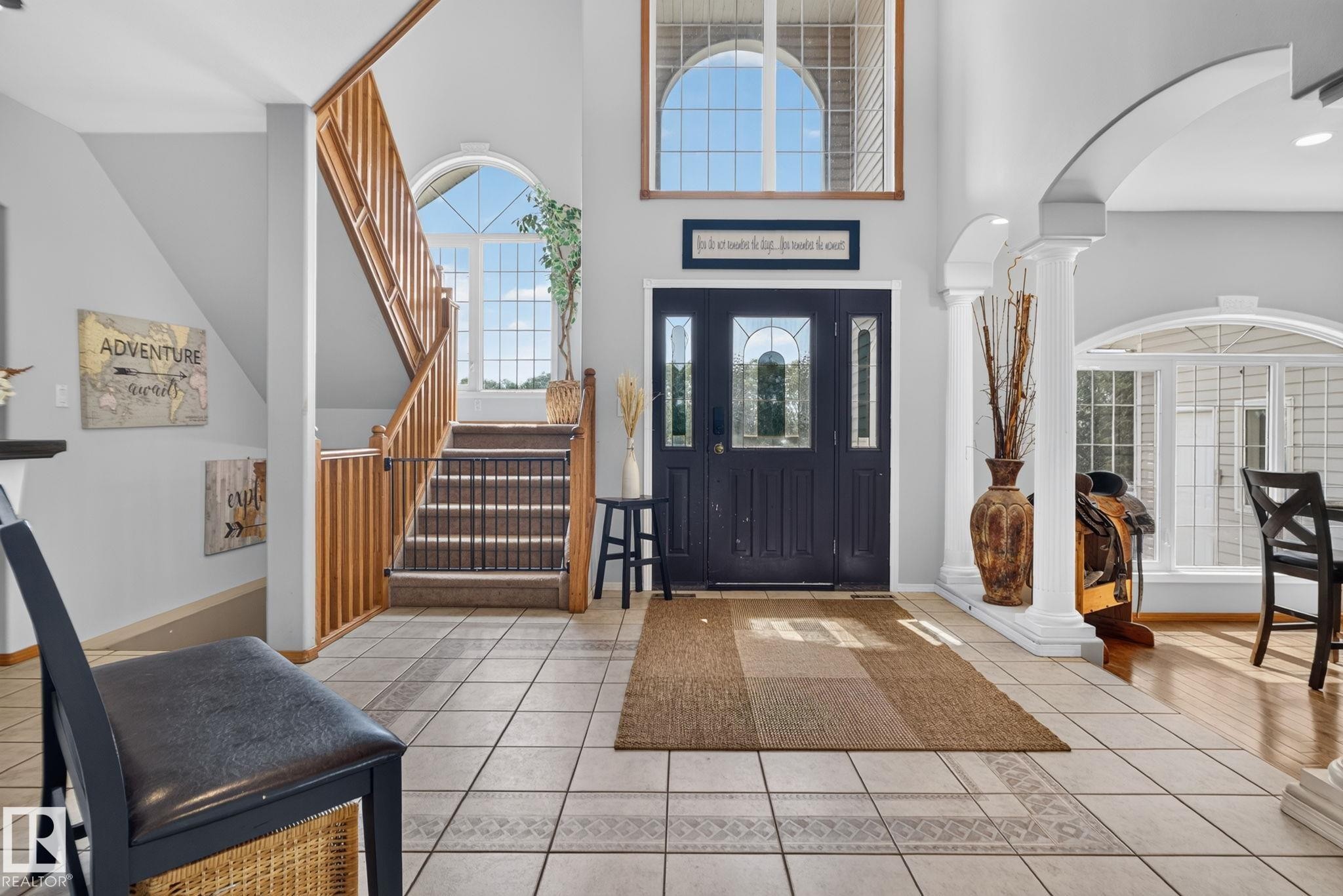 Two-story foyer featuring tile flooring, a dark paneled front door with decorative glass inserts, an arched transom window, a wooden staircase with carpeted treads, and an arched entryway with columns - 50336 Range Road 280, Rural Leduc County, AB - Indoor Photo Showing Other Room