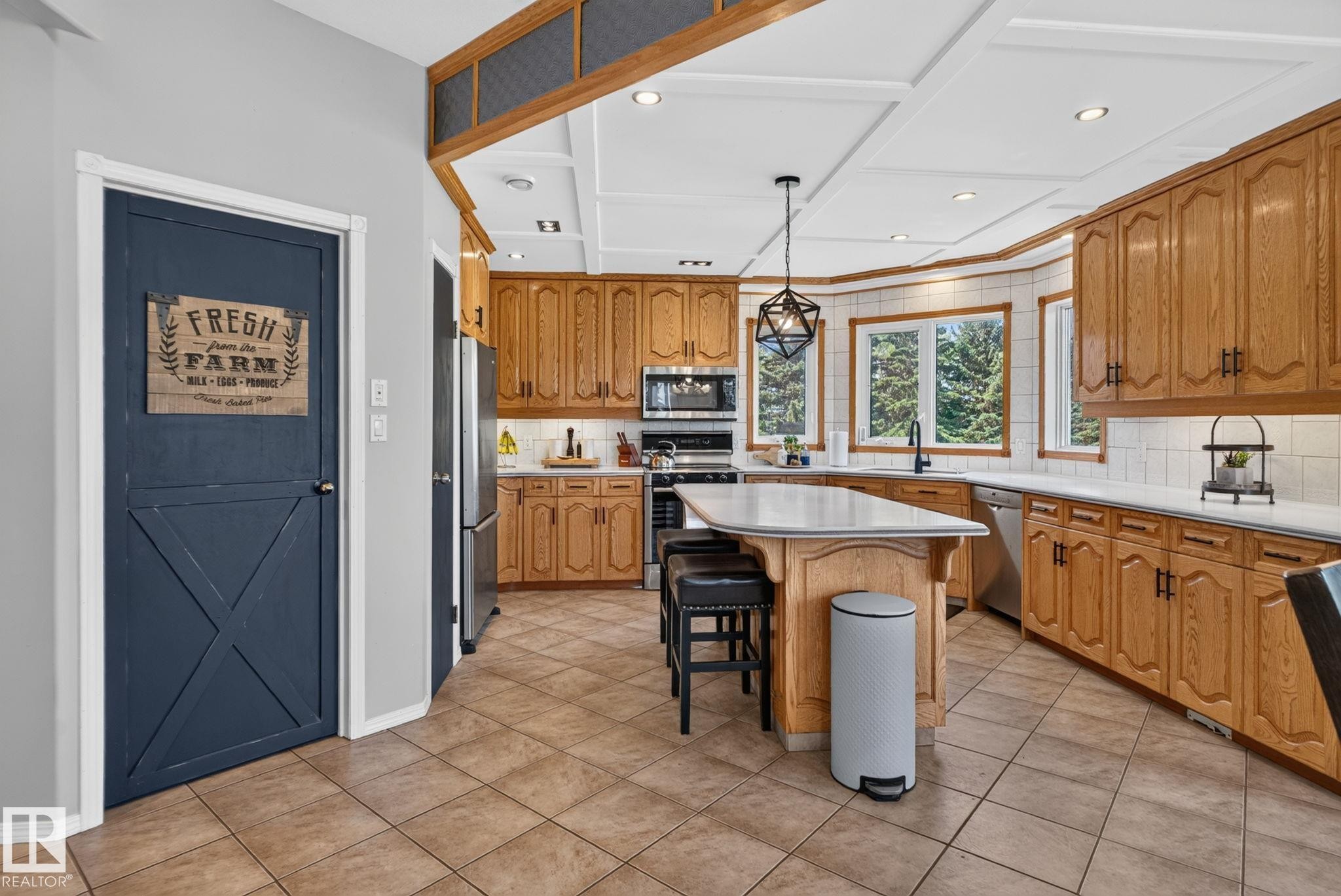 Spacious kitchen featuring natural wood cabinetry, light-toned tile flooring, and a large center island with seating - 50336 Range Road 280, Rural Leduc County, AB - Indoor Photo Showing Kitchen