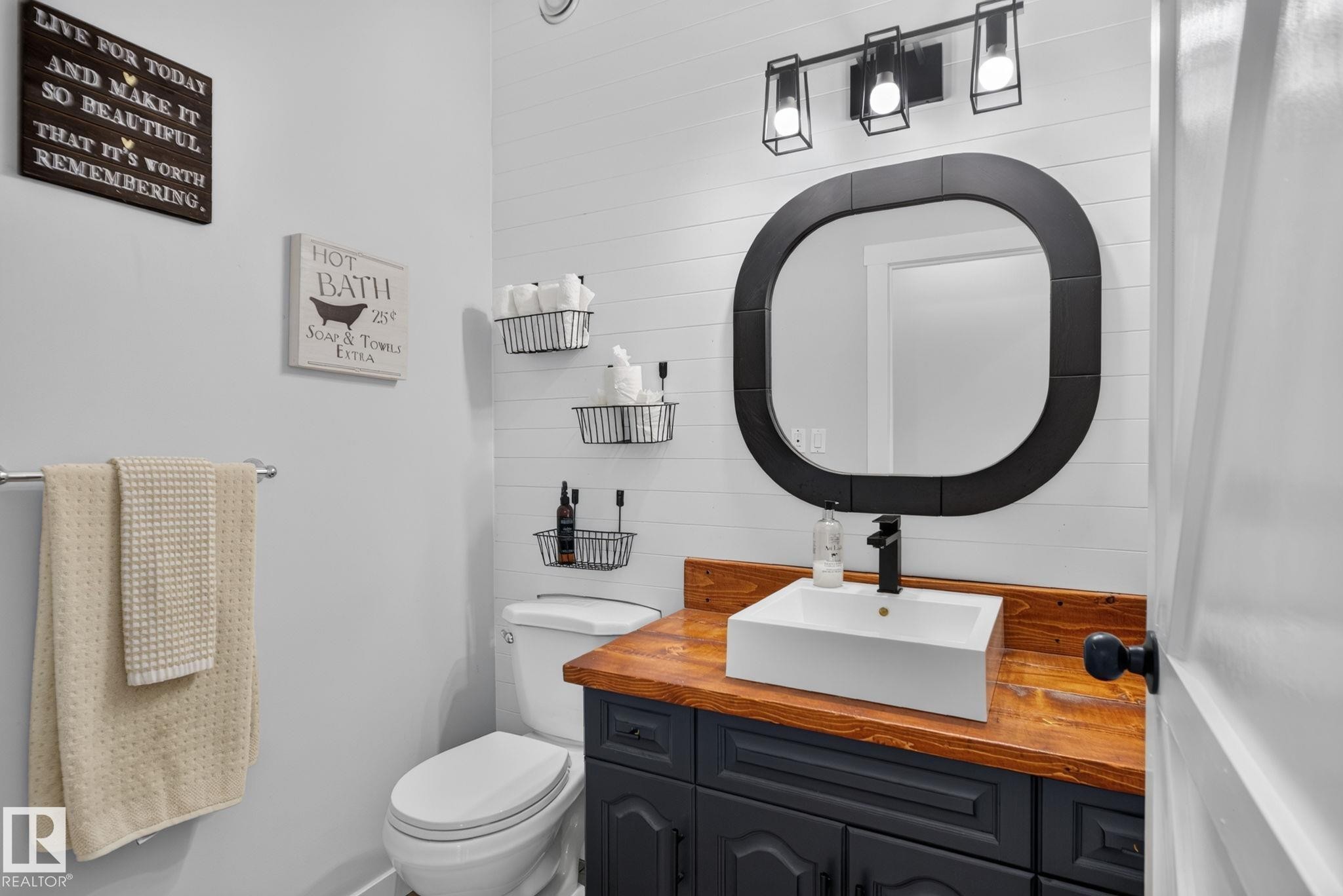 Modern bathroom featuring a striking rounded black-framed mirror, vessel sink with chrome faucet mounted on a warm wood-finish vanity, and black cabinetry with ample storage - 50336 Range Road 280, Rural Leduc County, AB - Indoor Photo Showing Bathroom