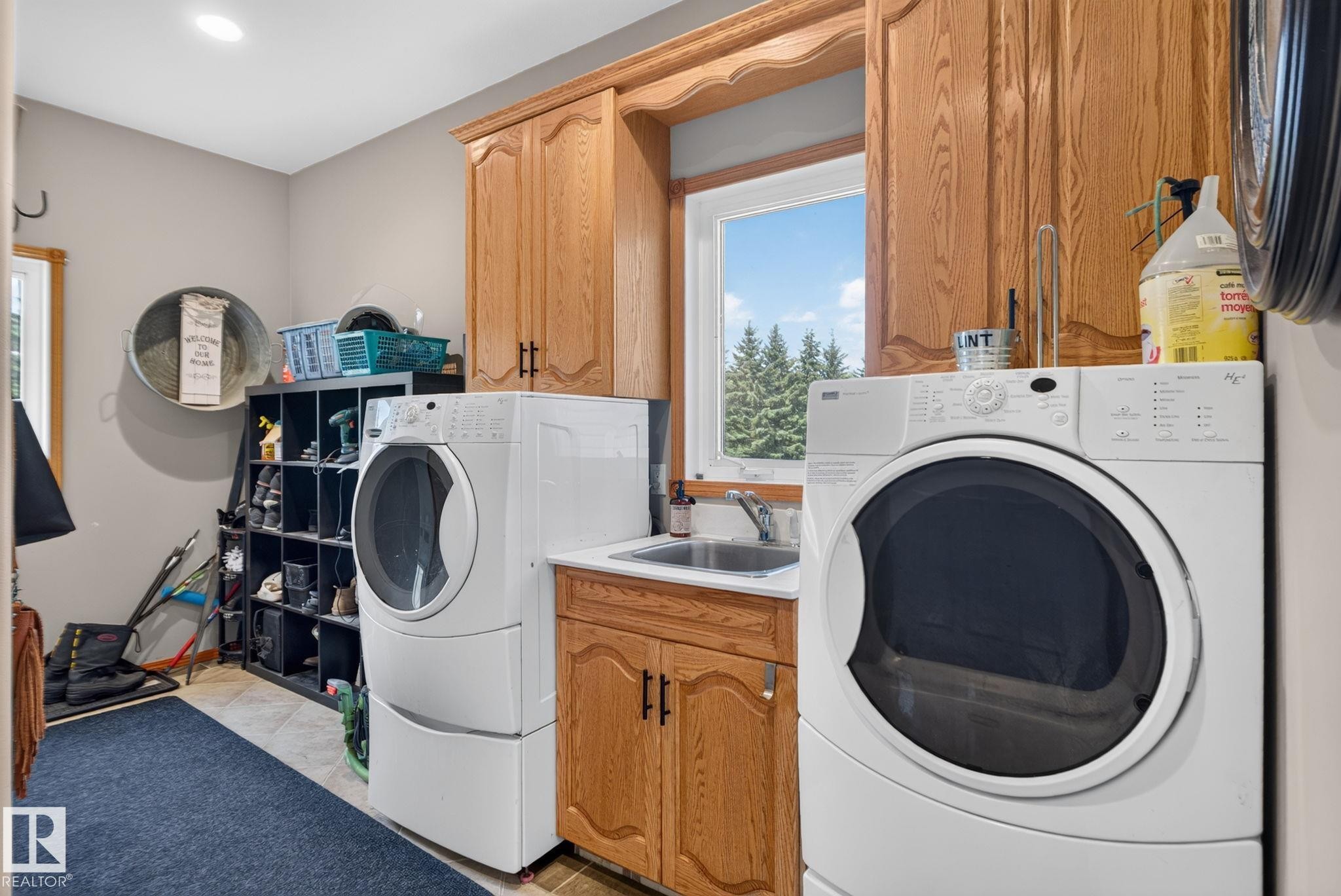 Dedicated laundry space featuring a utility sink, wood-finish cabinetry, and a window with outdoor scenery - 50336 Range Road 280, Rural Leduc County, AB - Indoor Photo Showing Laundry Room