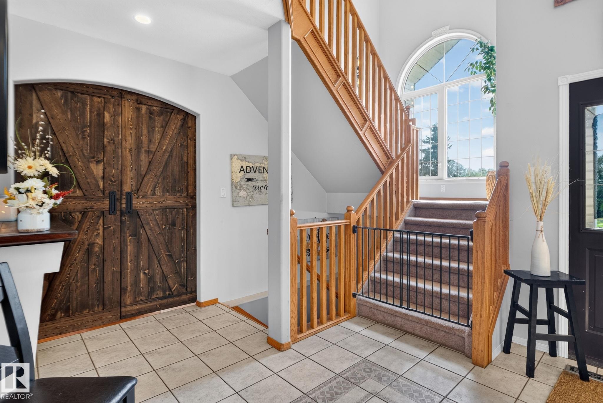 Foyer featuring a grand staircase with wood railings, an arched window, and barn doors with dark hardware - 50336 Range Road 280, Rural Leduc County, AB - Indoor Photo Showing Other Room
