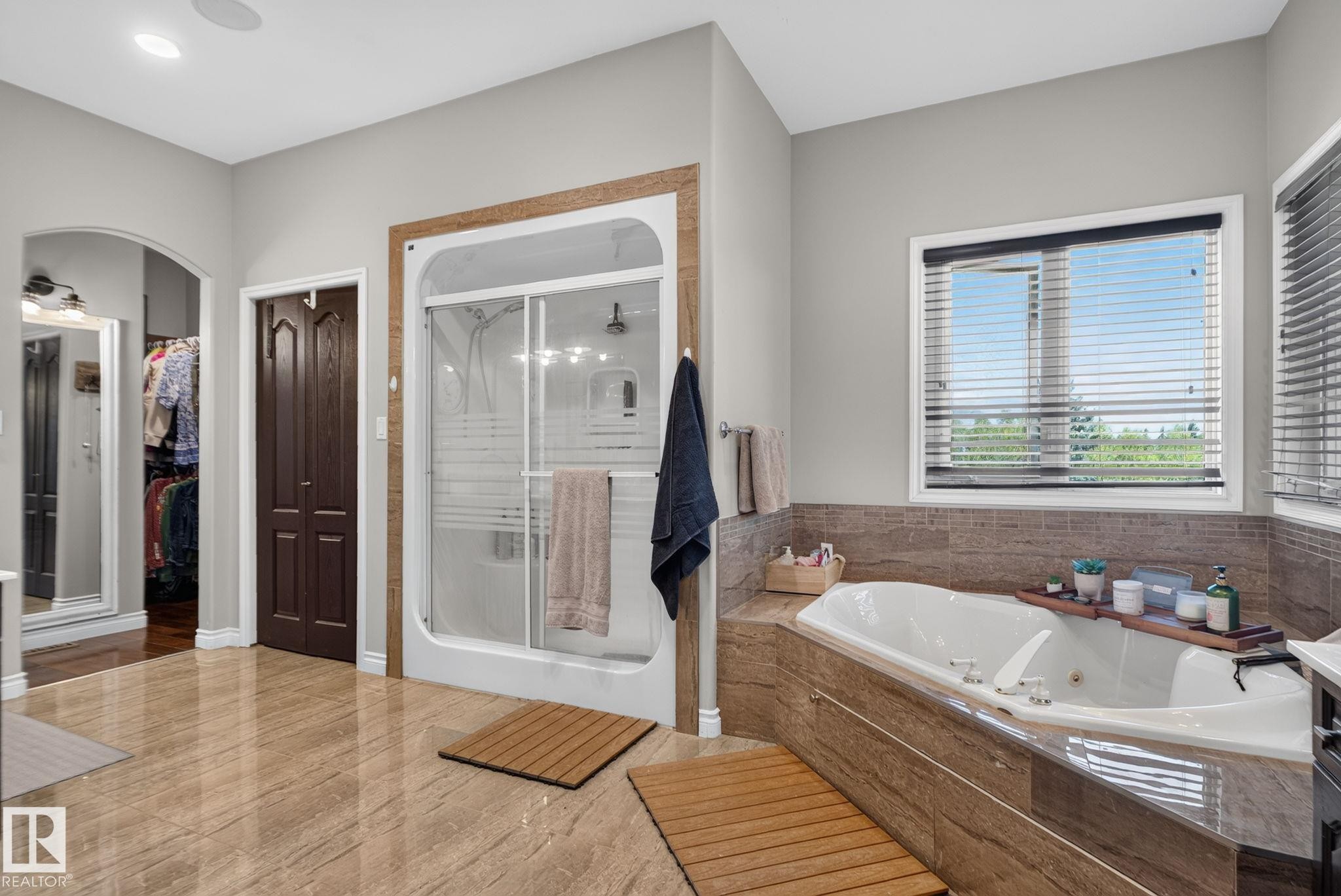 Spacious bathroom featuring a built-in soaking tub with stone-finish surround, a standing shower with sliding glass doors, and light-toned tile flooring - 50336 Range Road 280, Rural Leduc County, AB - Indoor Photo Showing Bathroom