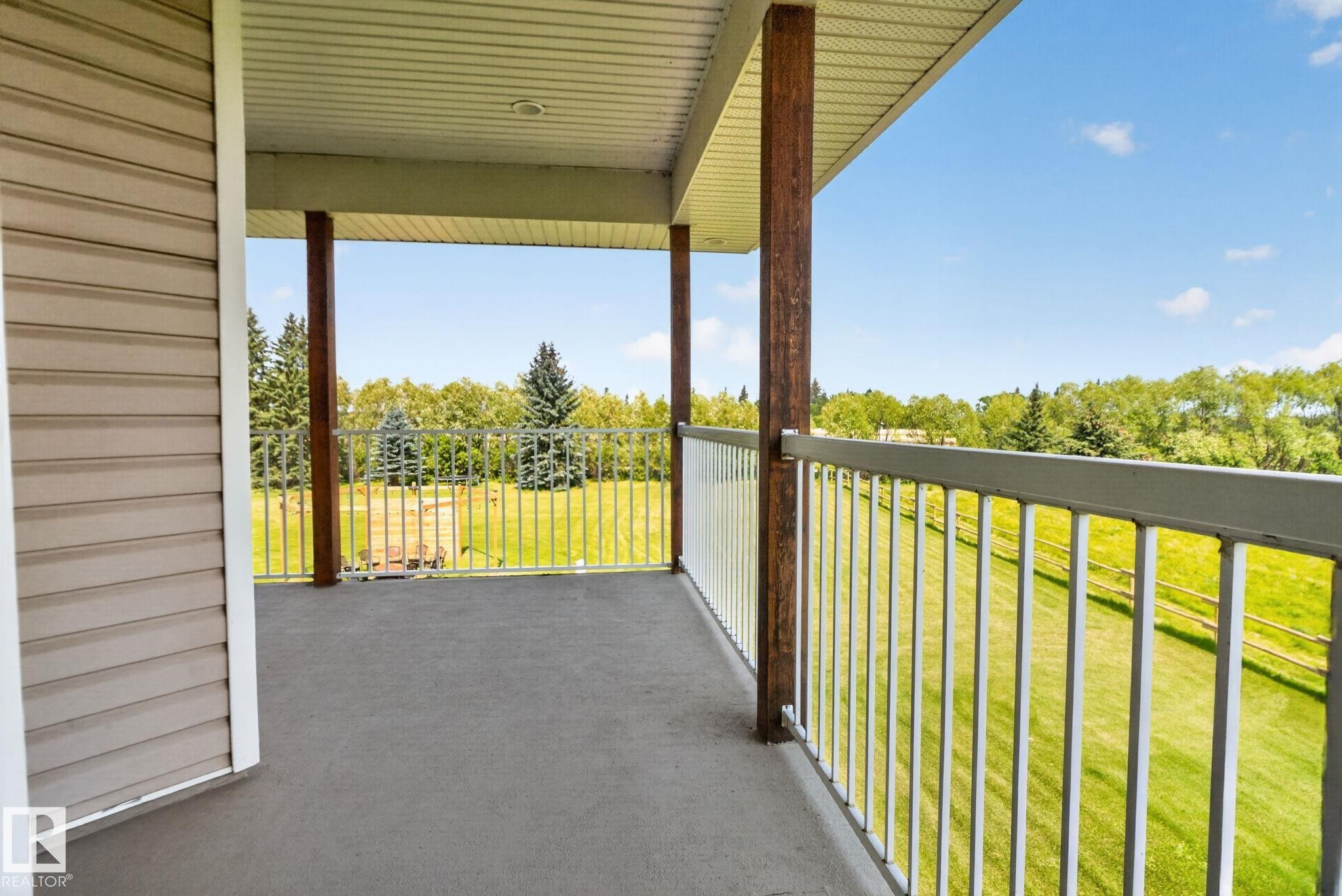 Expansive covered deck with composite decking, metal railings, and support columns overlooking manicured grounds and tree-lined landscape - 50336 Range Road 280, Rural Leduc County, AB - Outdoor With Exterior