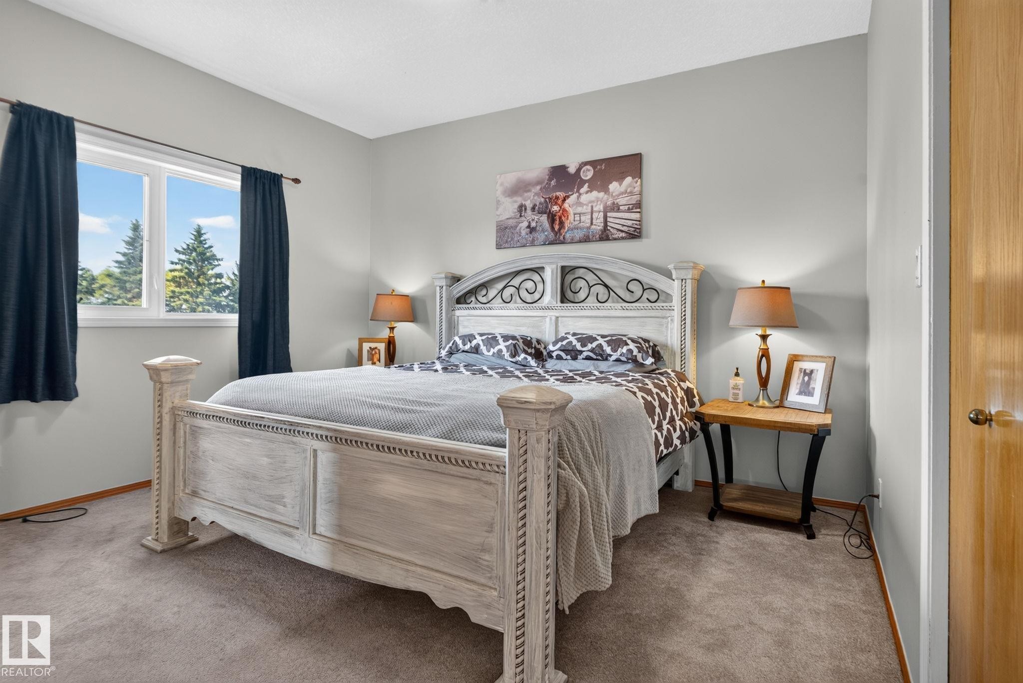 Carpeted bedroom featuring a large window, light gray walls, and a light wood-finish door - 50336 Range Road 280, Rural Leduc County, AB - Indoor Photo Showing Bedroom