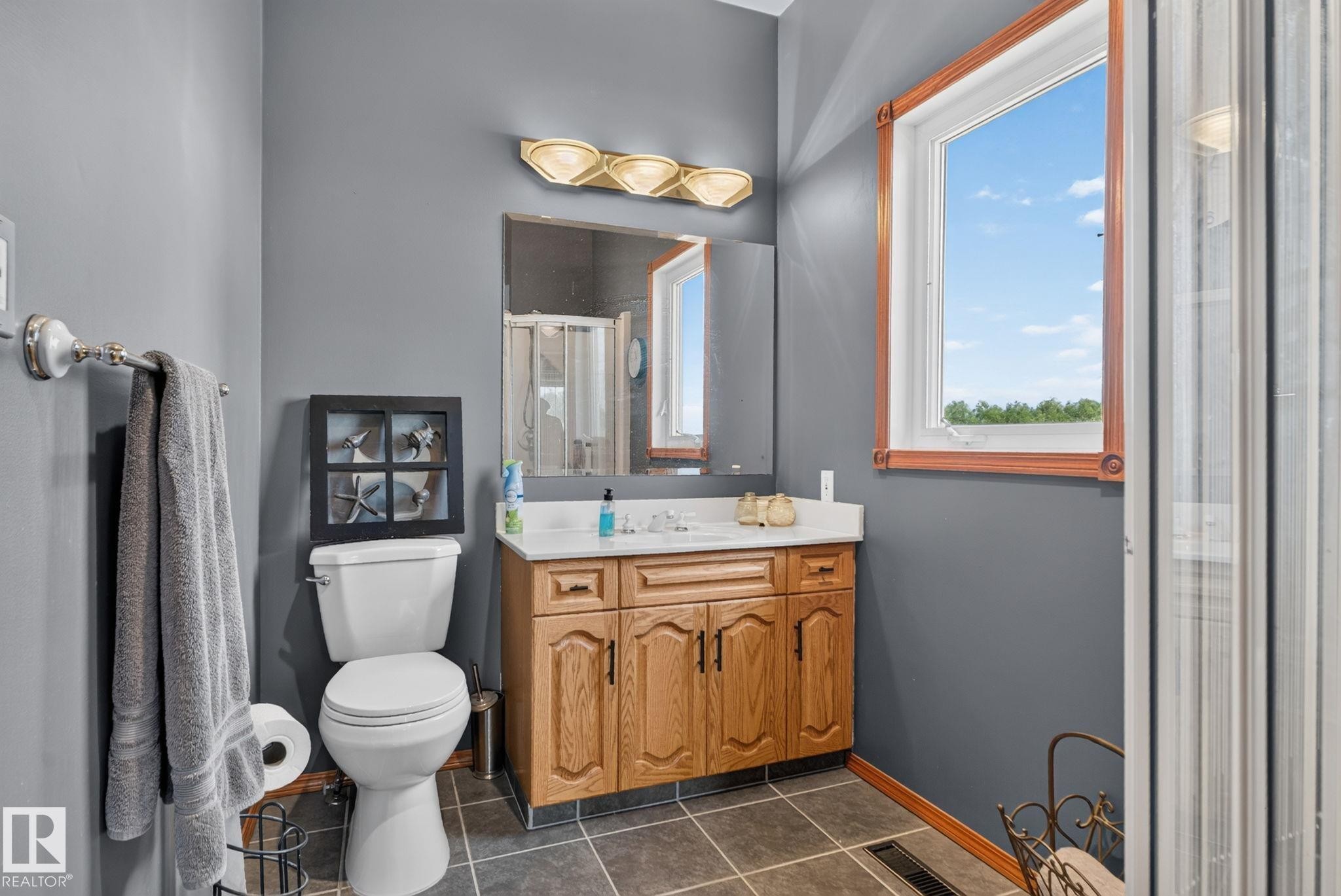 Bathroom featuring a single window with wood trim, a wood-finish vanity with a white countertop, a wall-mounted mirror, and a shower enclosure - 50336 Range Road 280, Rural Leduc County, AB - Indoor Photo Showing Bathroom