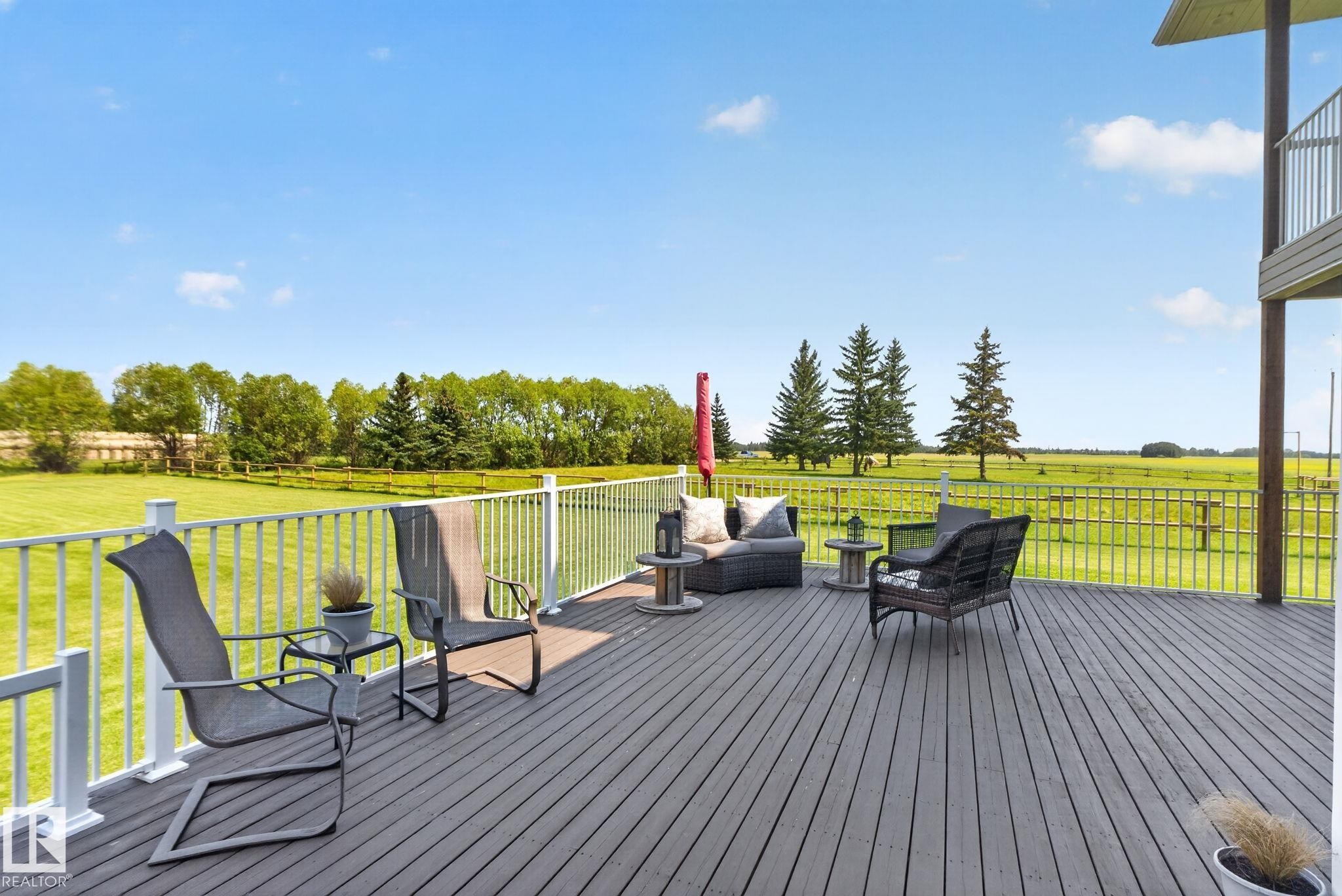 Expansive composite deck featuring horizontal wood-finish decking, white aluminum railing, and multiple seating zones overlooking manicured grounds - 50336 Range Road 280, Rural Leduc County, AB - Outdoor With Exterior