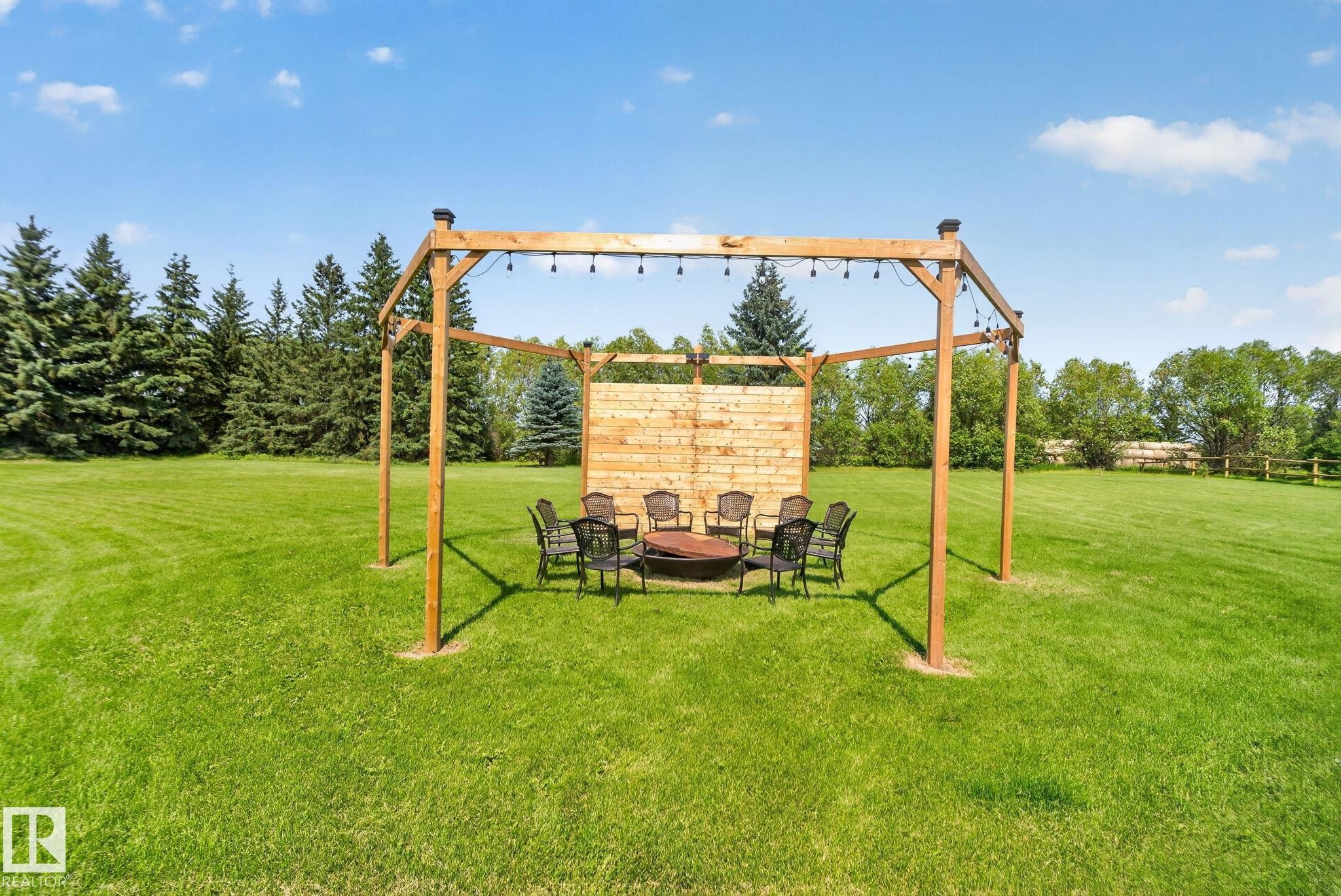 Expansive green lawn with a wooden pergola featuring string lighting and a built-in fire pit - 50336 Range Road 280, Rural Leduc County, AB - Outdoor