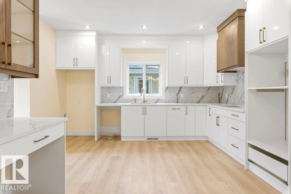 Bright kitchen featuring white cabinetry with gold-tone hardware, a light wood-finish floor, and a white countertop with a matching backsplash - 10323 79 Street Nw, Edmonton, AB - Indoor Photo Showing Kitchen